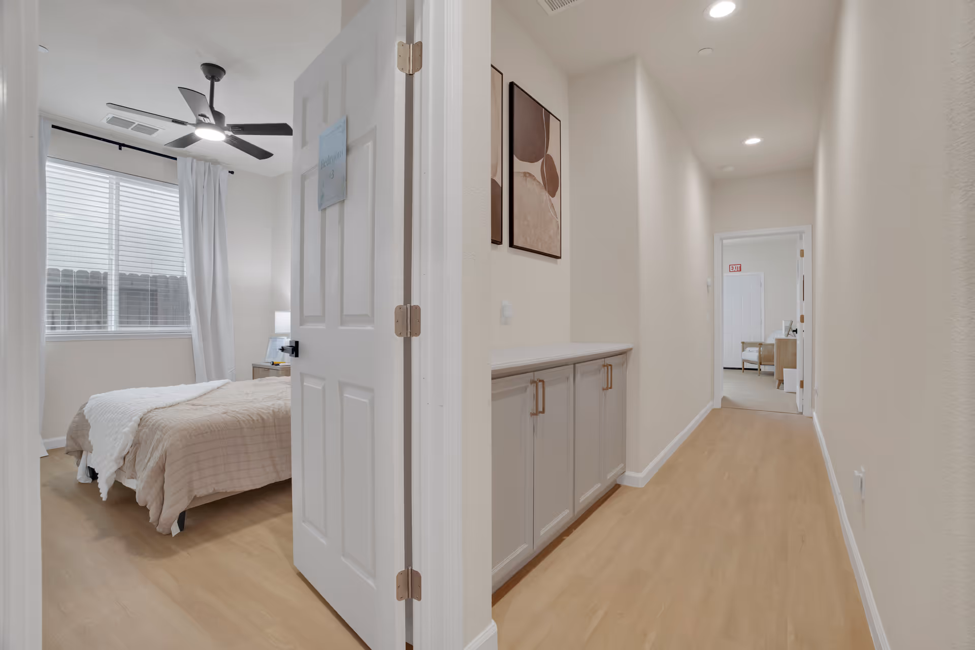 A hallway view into a bedroom with a bed, window, and built-in cabinets.