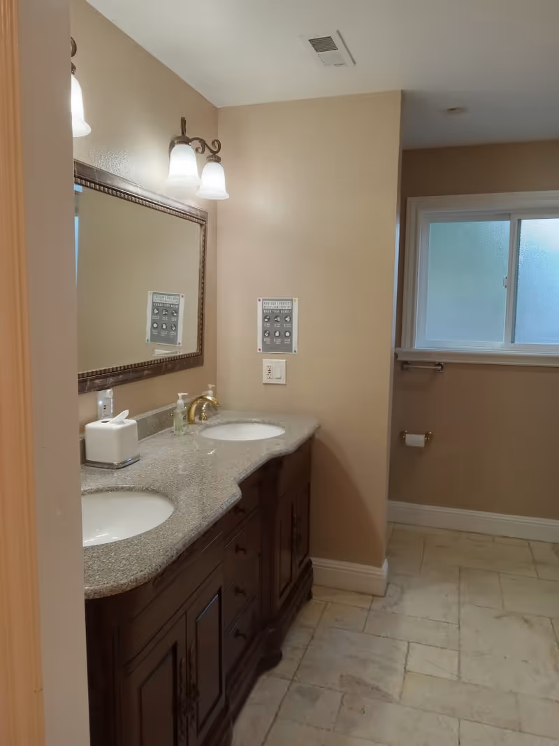 Interior bathroom with dual sinks, granite countertop, framed mirror, and frosted window.