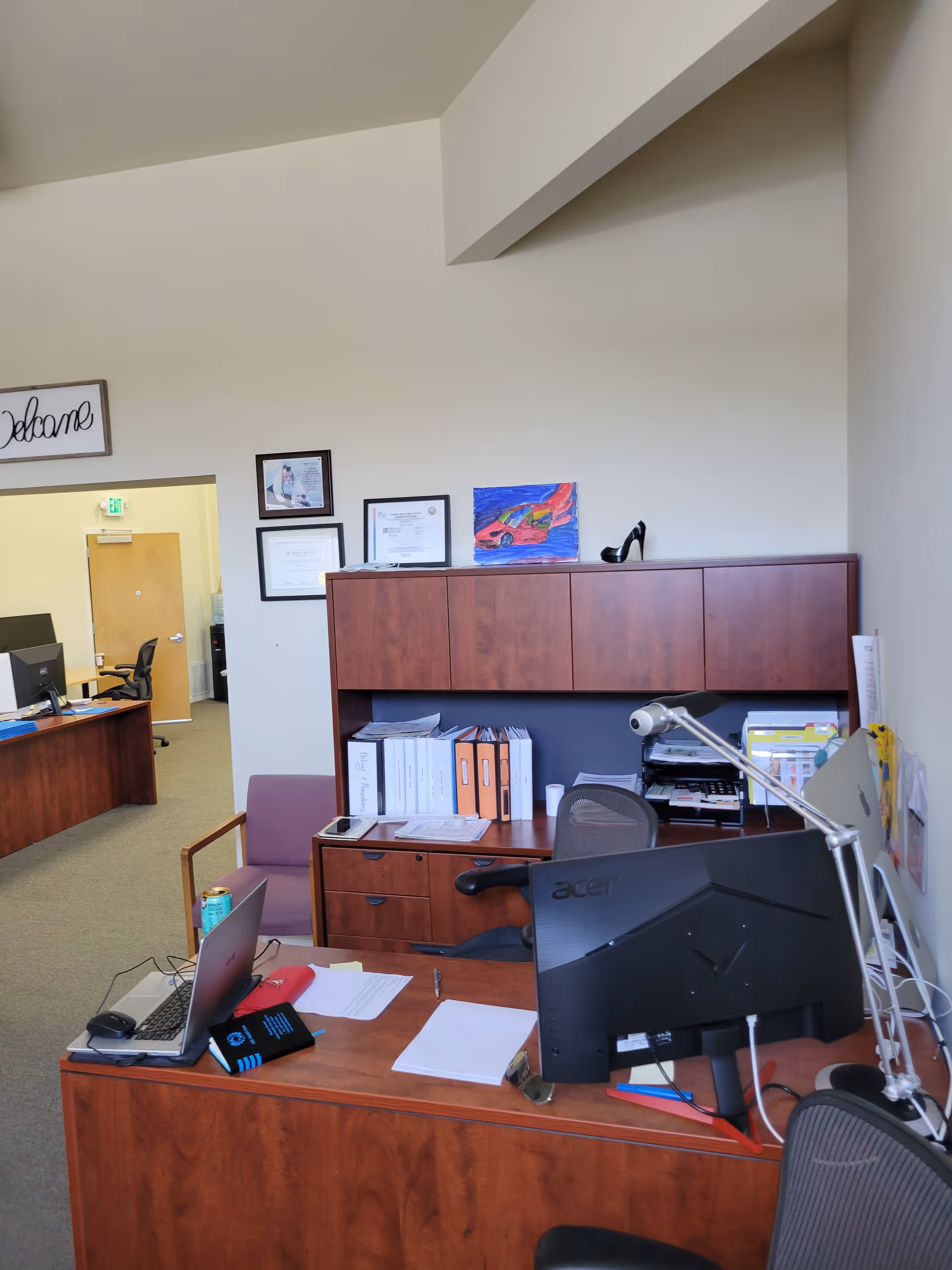 Office workspace with desks, computers, cabinets, and filing shelves in a senior care facility.