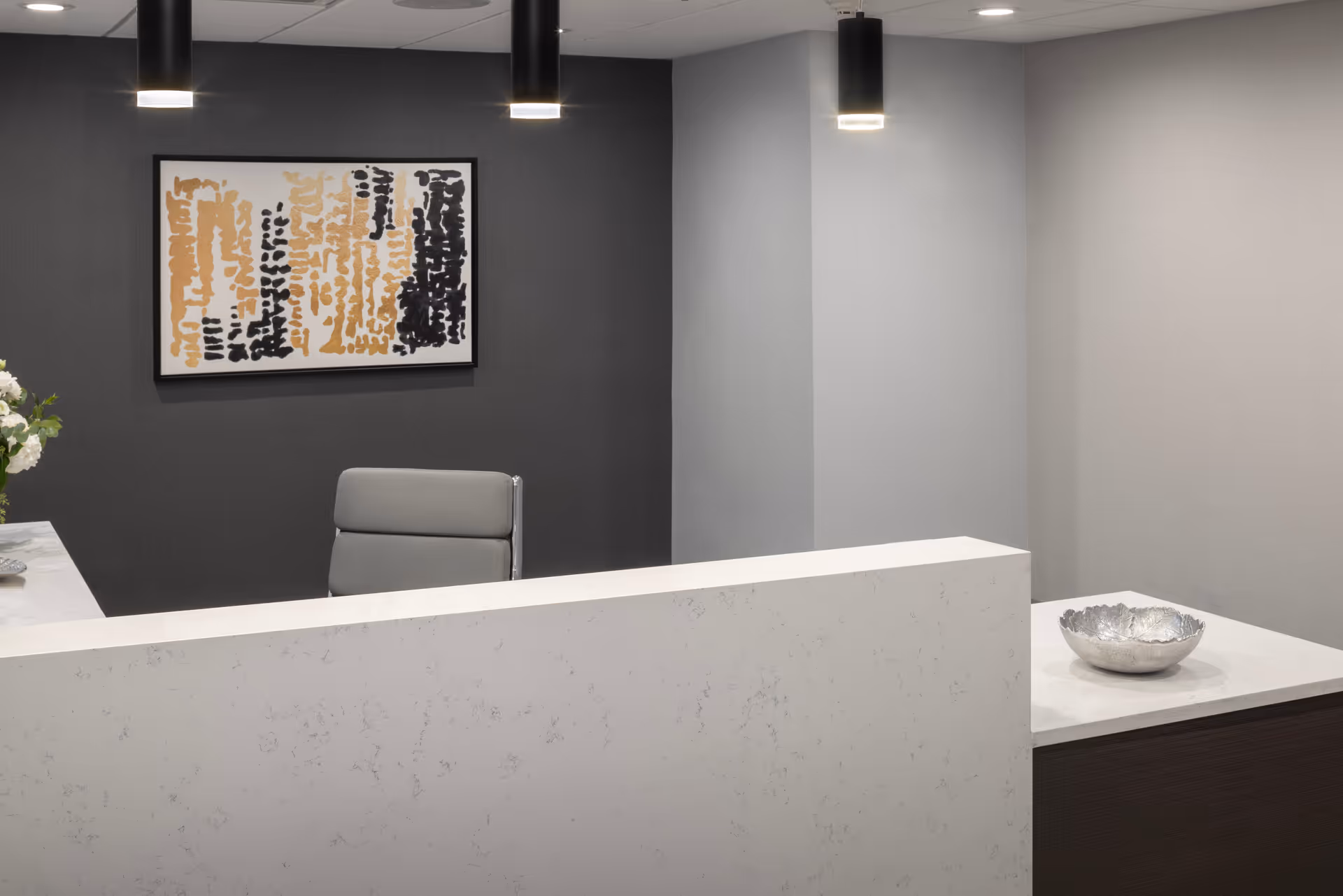 Reception desk with a chair, abstract art, and pendant lights in a neutral interior lobby.