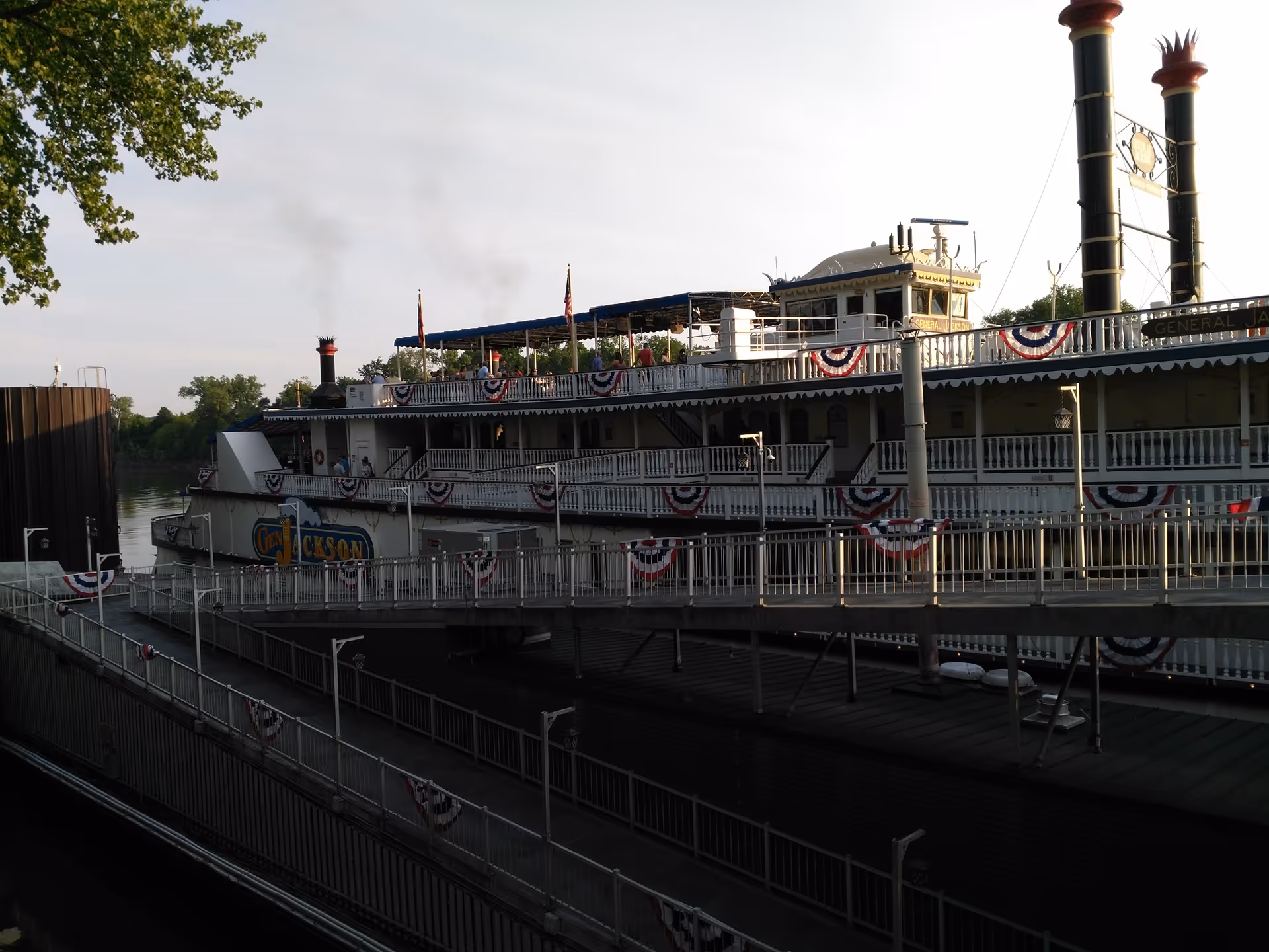 A decorated riverboat steamboat docked at a pier with bunting along the rails