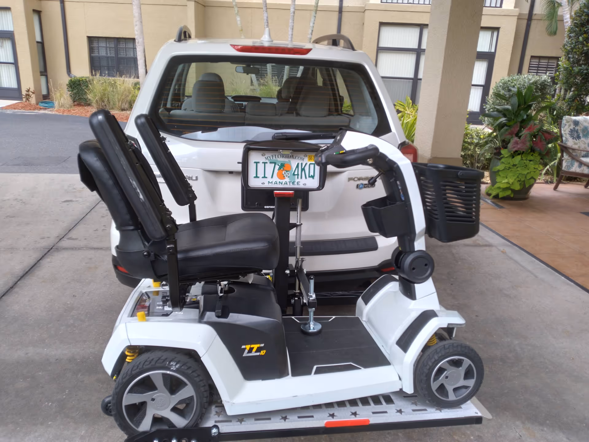 A white mobility scooter on a platform outside a beige senior living building.