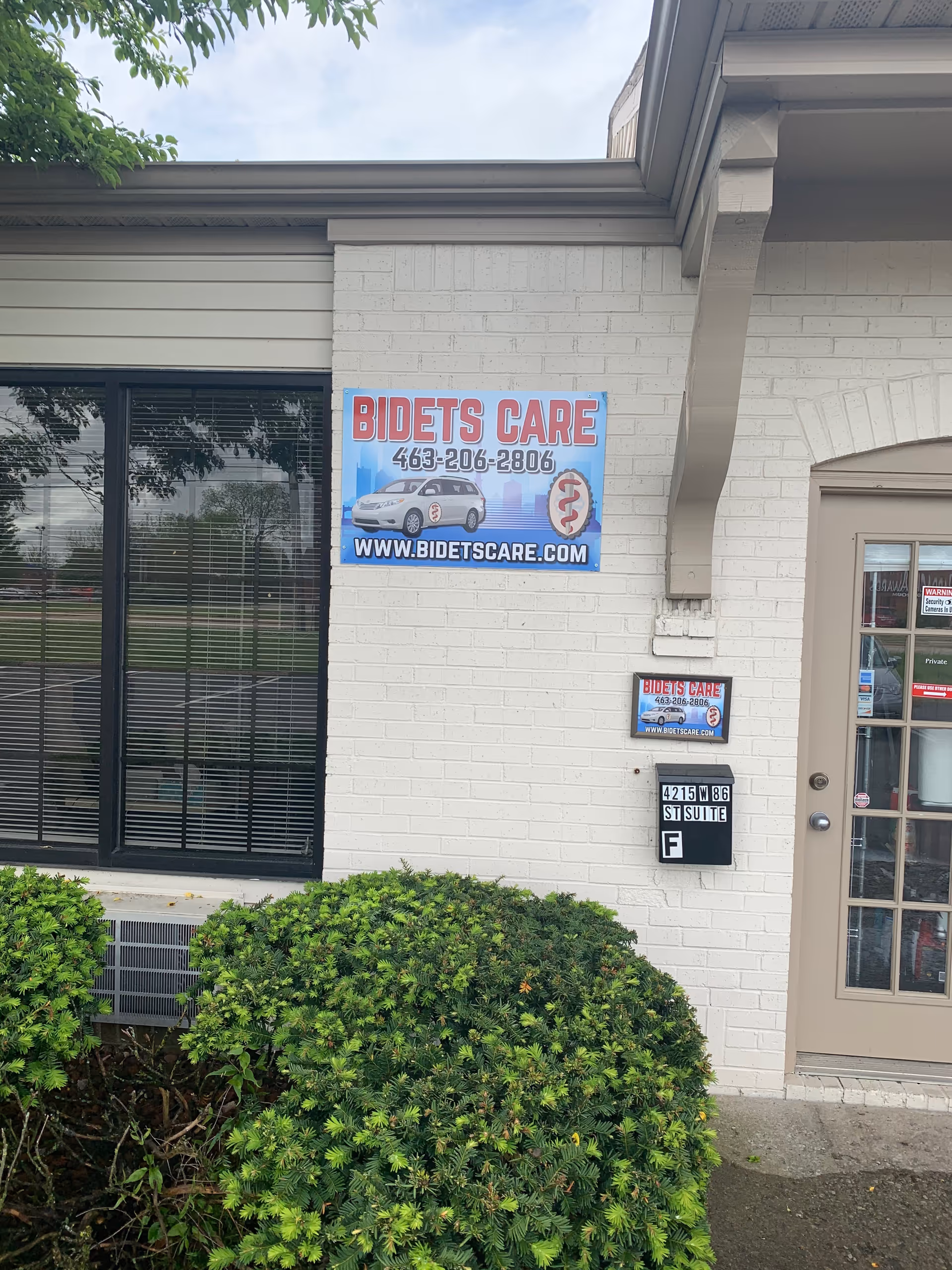 Exterior of Bidets Care LLC building with sign, door, and greenery.