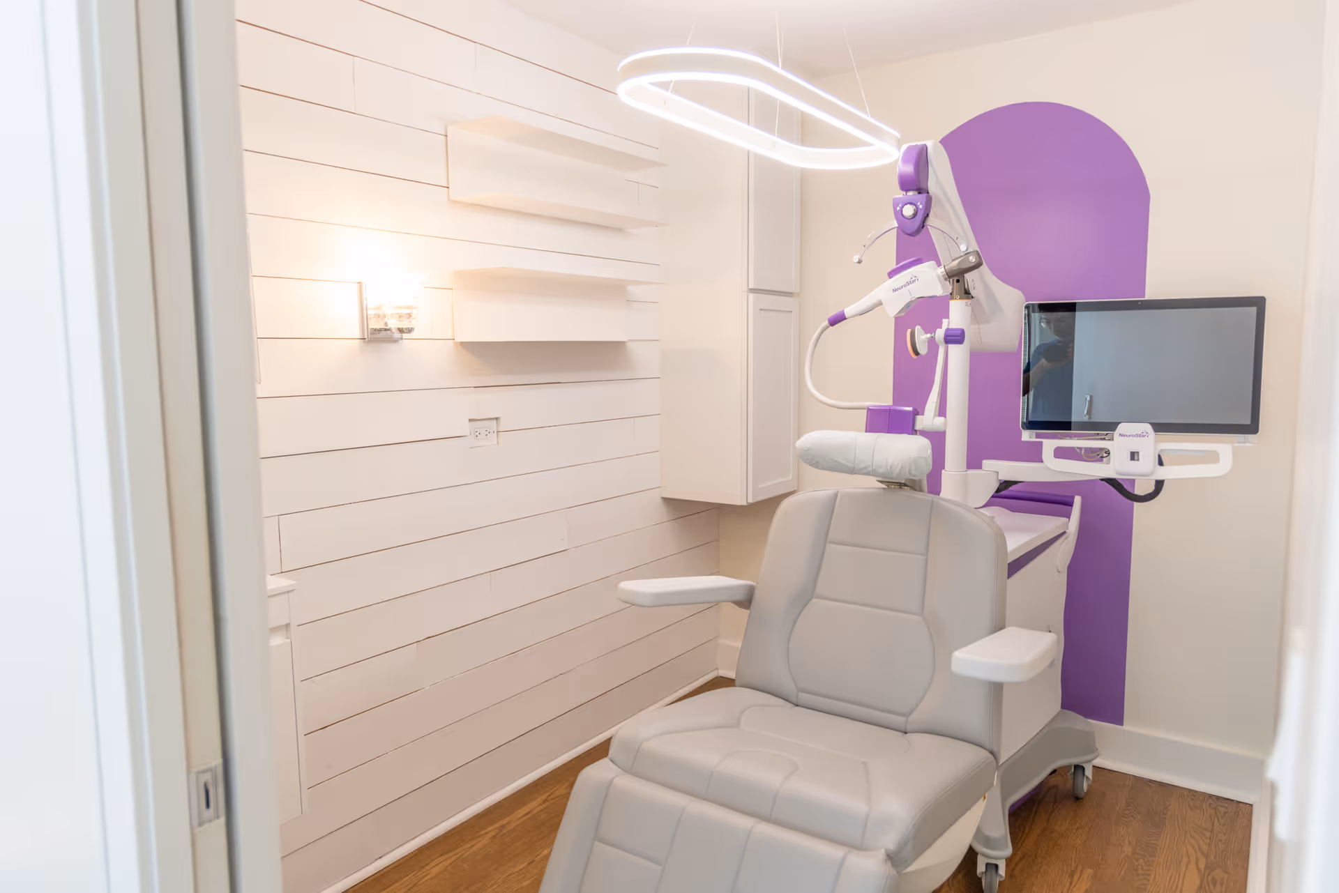 Modern medical treatment chair with monitor and purple wall in a clean clinic room.