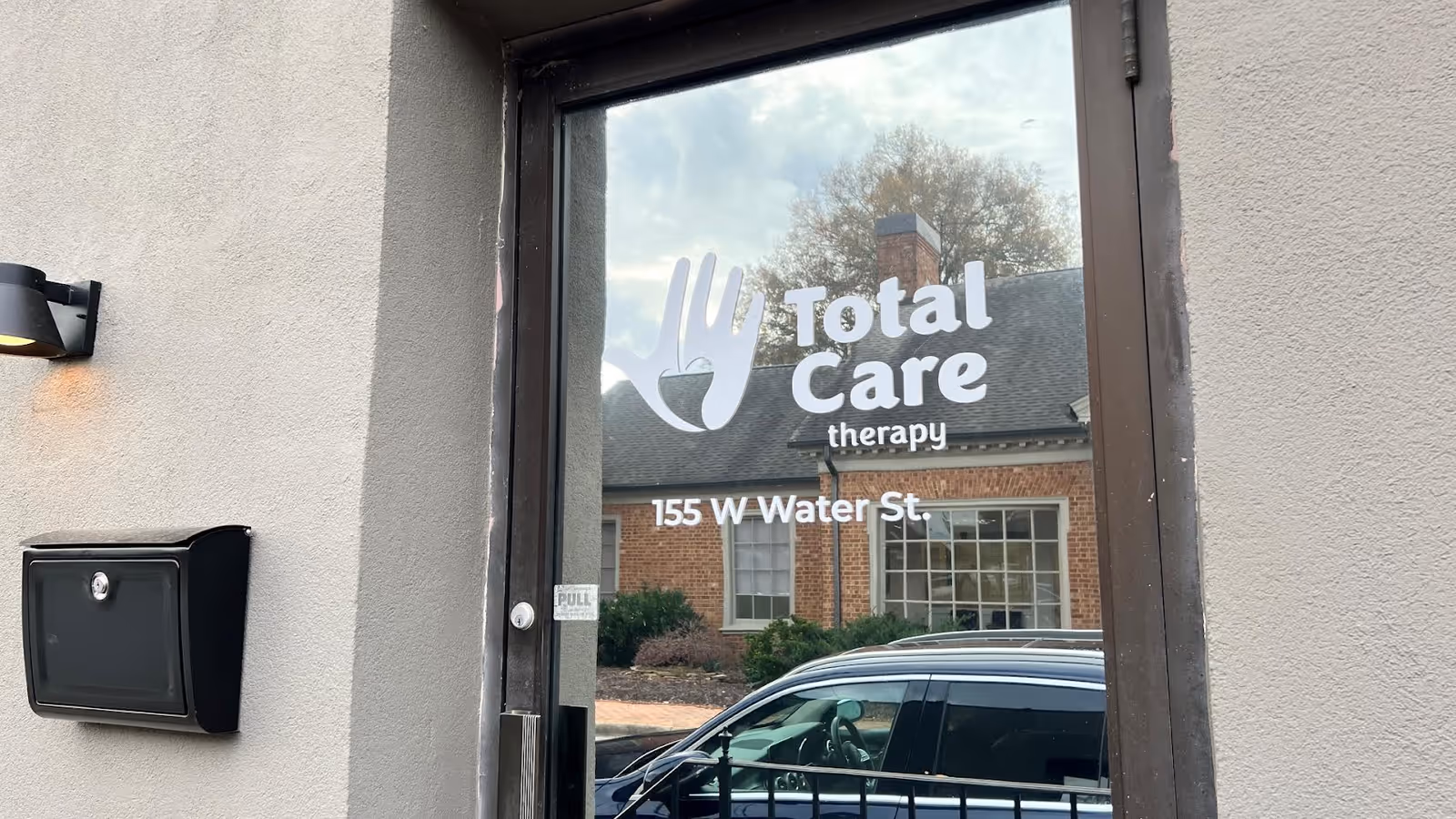 Glass entrance door of Total Care therapy building displaying logo and address