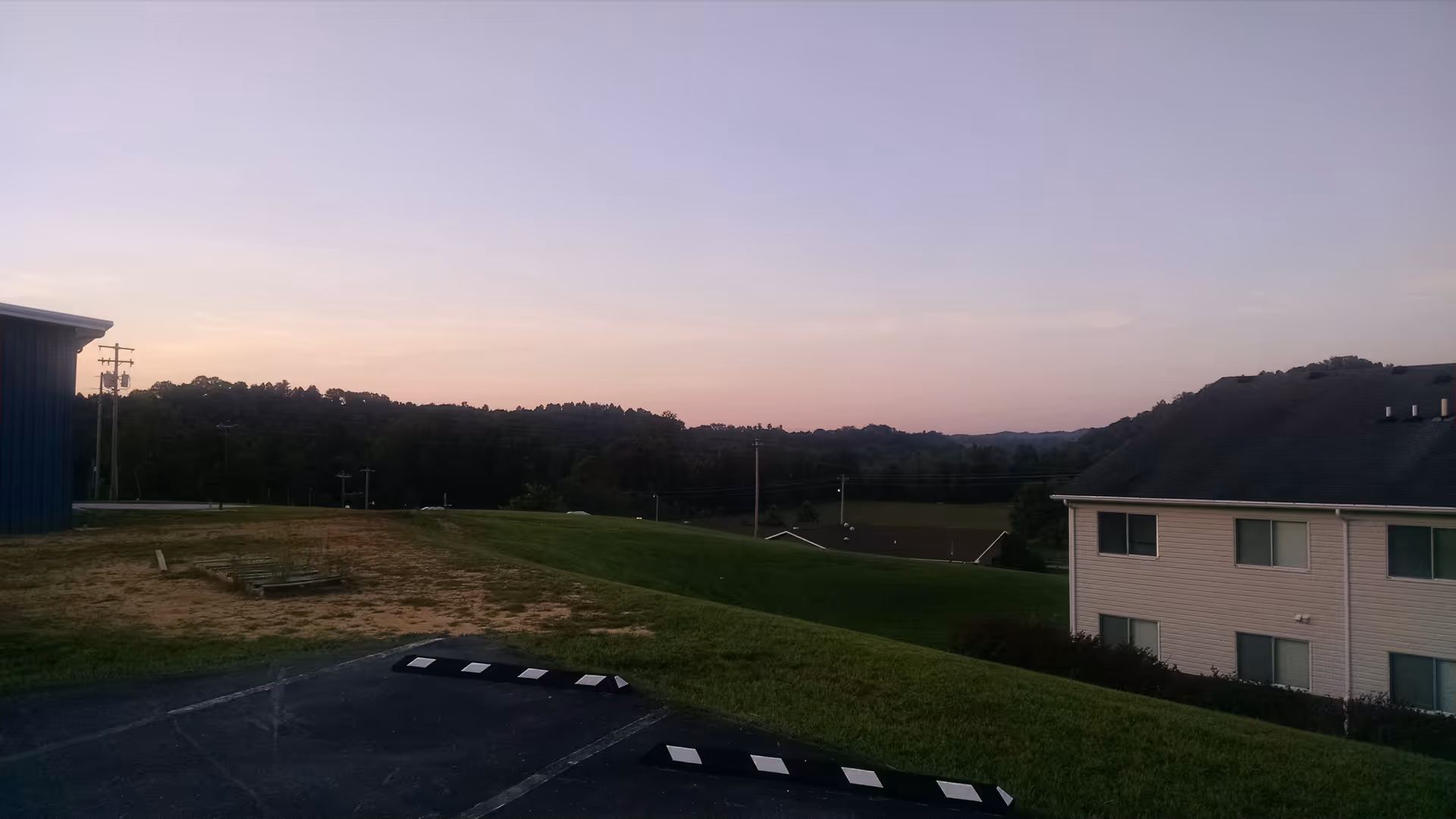 Sunset over grassy hills beside a two-story senior living facility and parking.