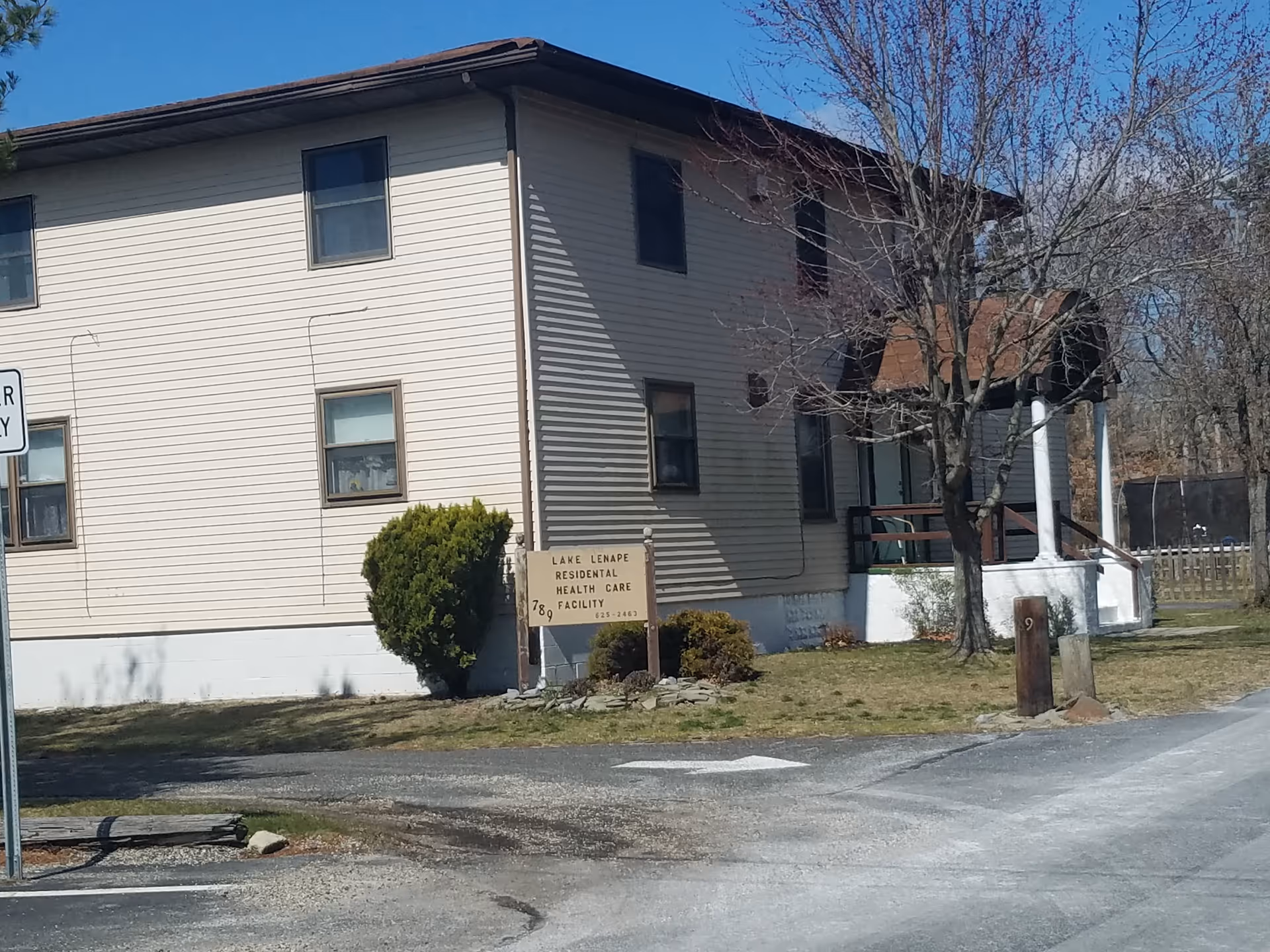 Exterior view of a two-story beige facility with a sign and leafless tree near the road.