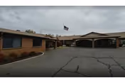 Front exterior of a single-story senior living facility with a driveway and flag.