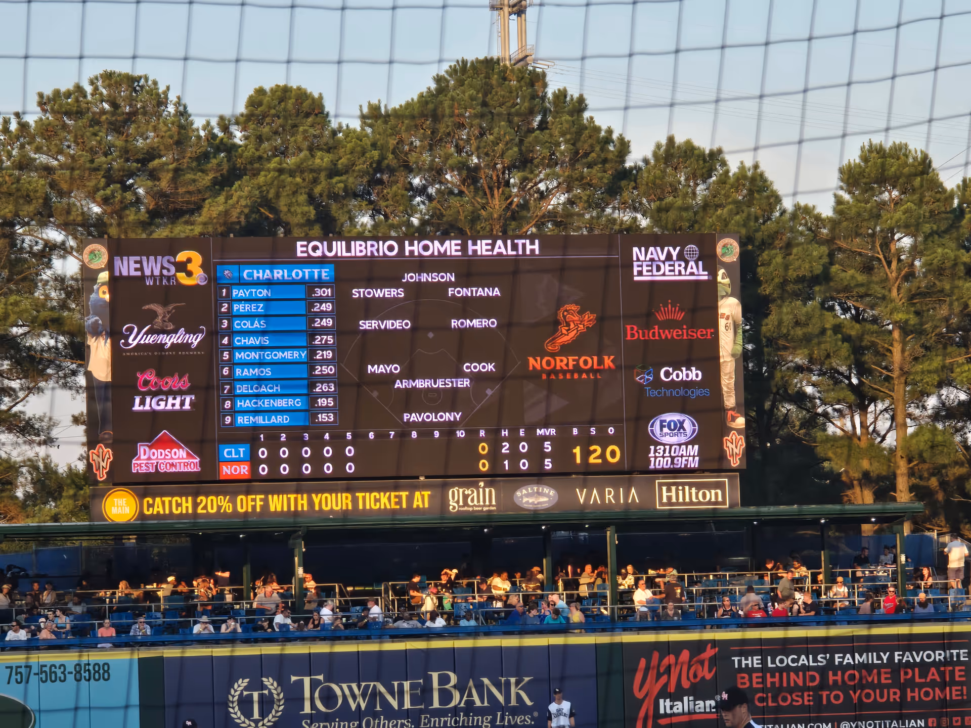 Outdoor baseball stadium scoreboard displays Equilibrio Home Health branding with spectators in the stands.