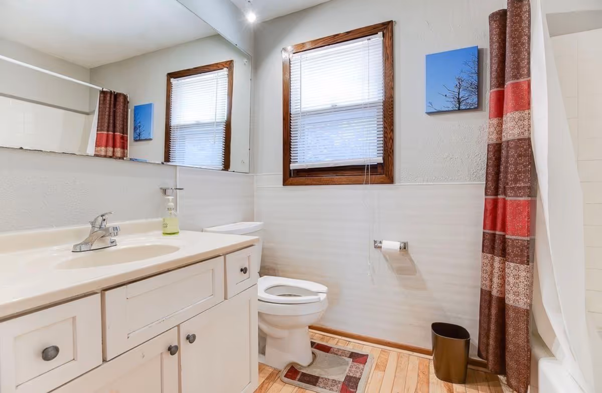Bright, clean bathroom with a white vanity, toilet, window, and striped shower curtain.