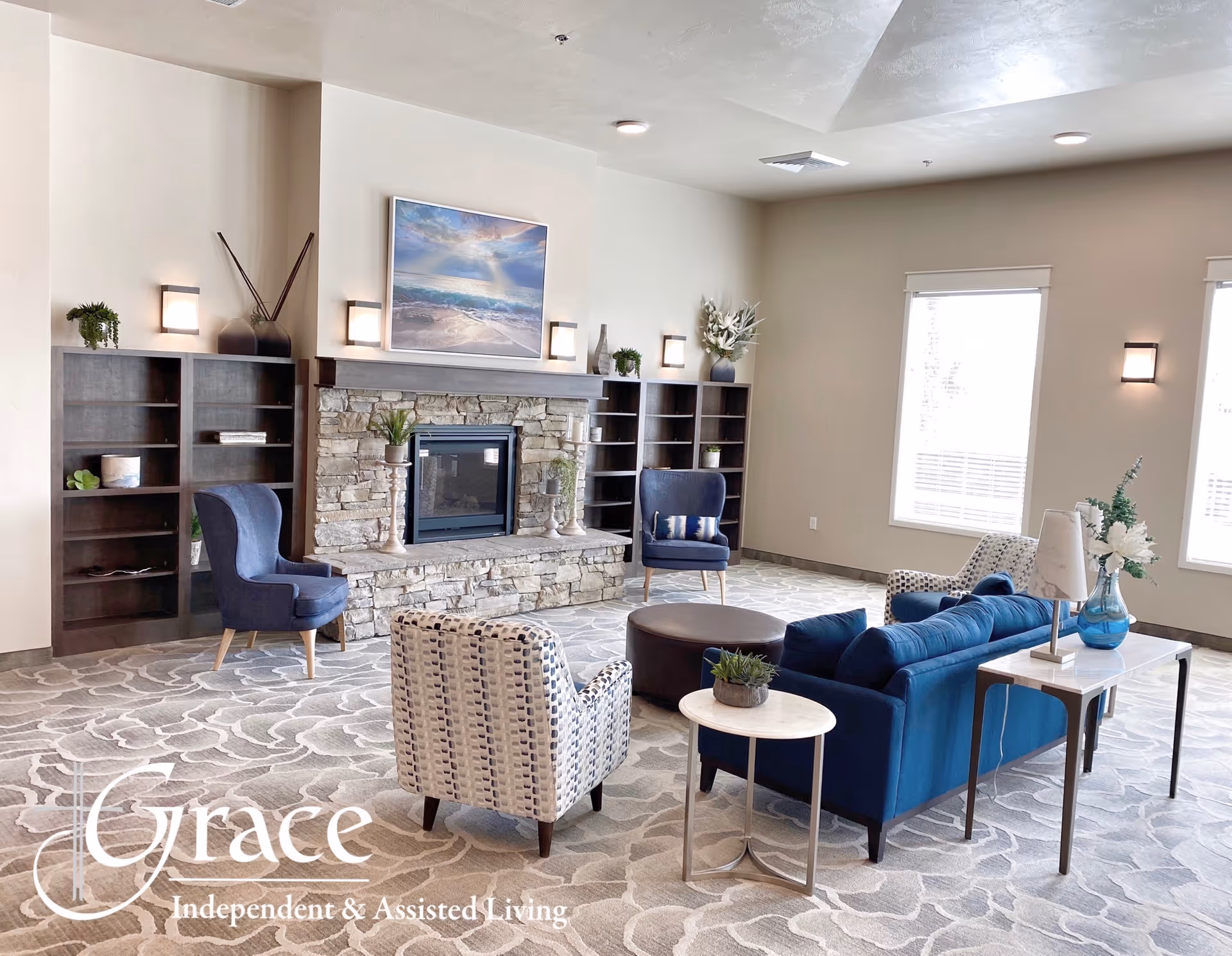 Spacious lounge with stone fireplace, blue seating, shelves, and decorative plants.