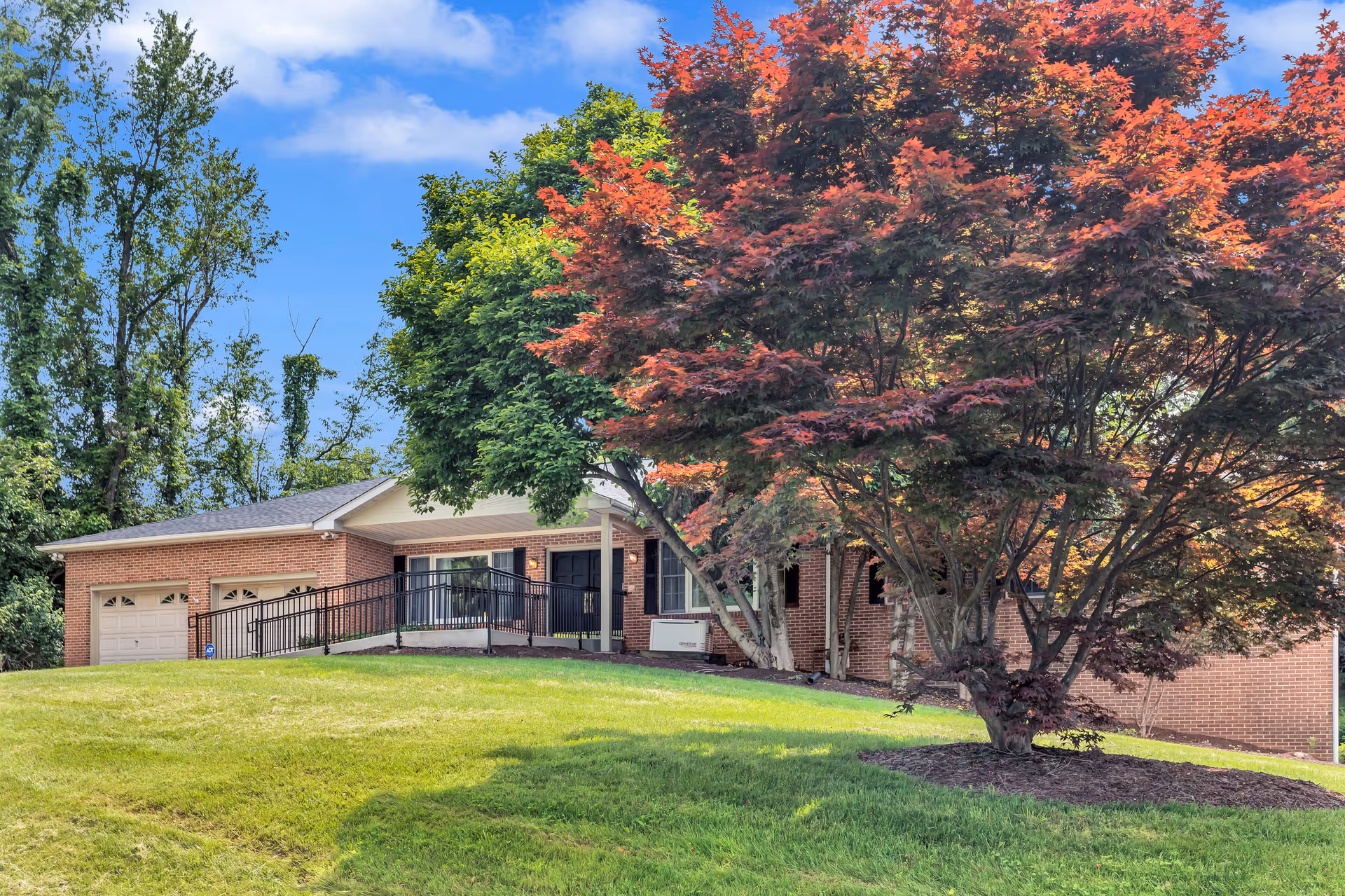 Brick single-story care home with a front ramp, double garage, and surrounding trees.