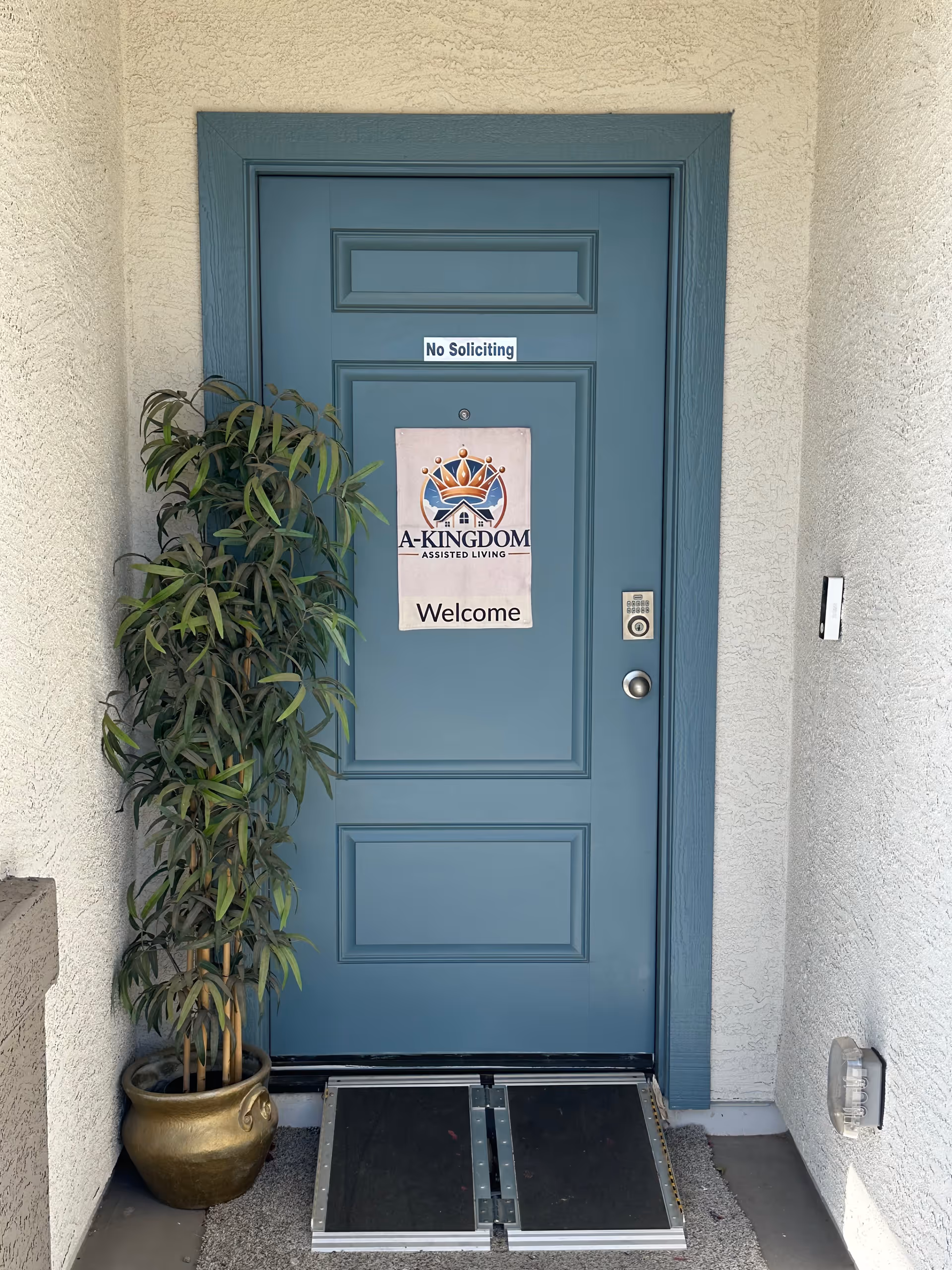 Blue front door of A-Kingdom Assisted Living with welcome sign and potted plant