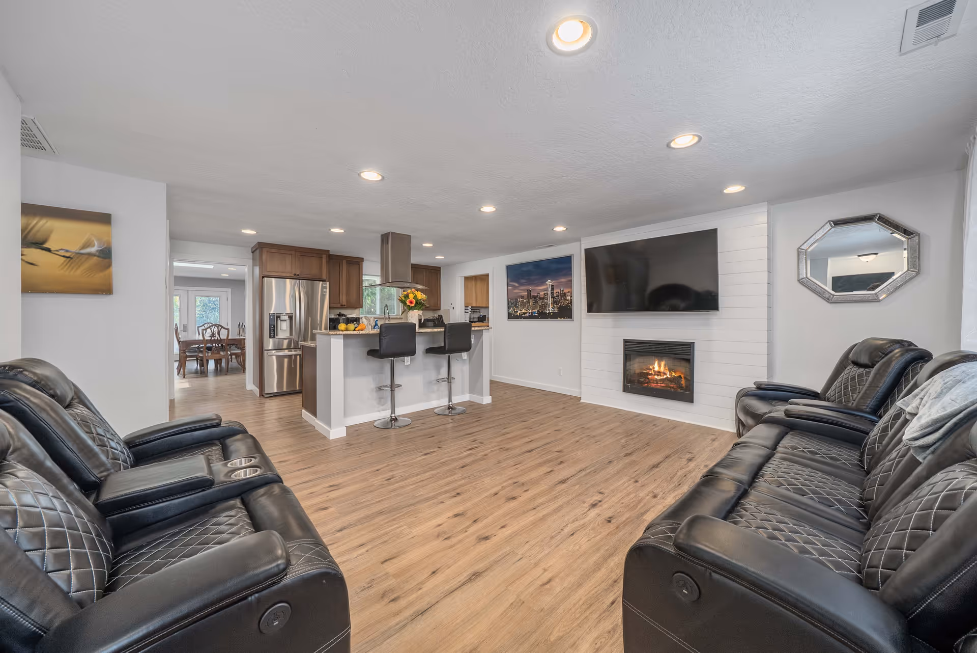 Open living area with leather recliners, a kitchen bar, fireplace, and large TV.