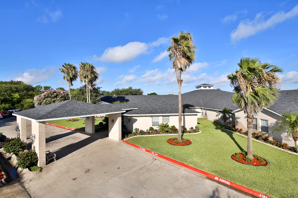 Exterior view of Edinburg Nursing and Rehabilitation Center with covered entrance, manicured lawn, and palm trees.