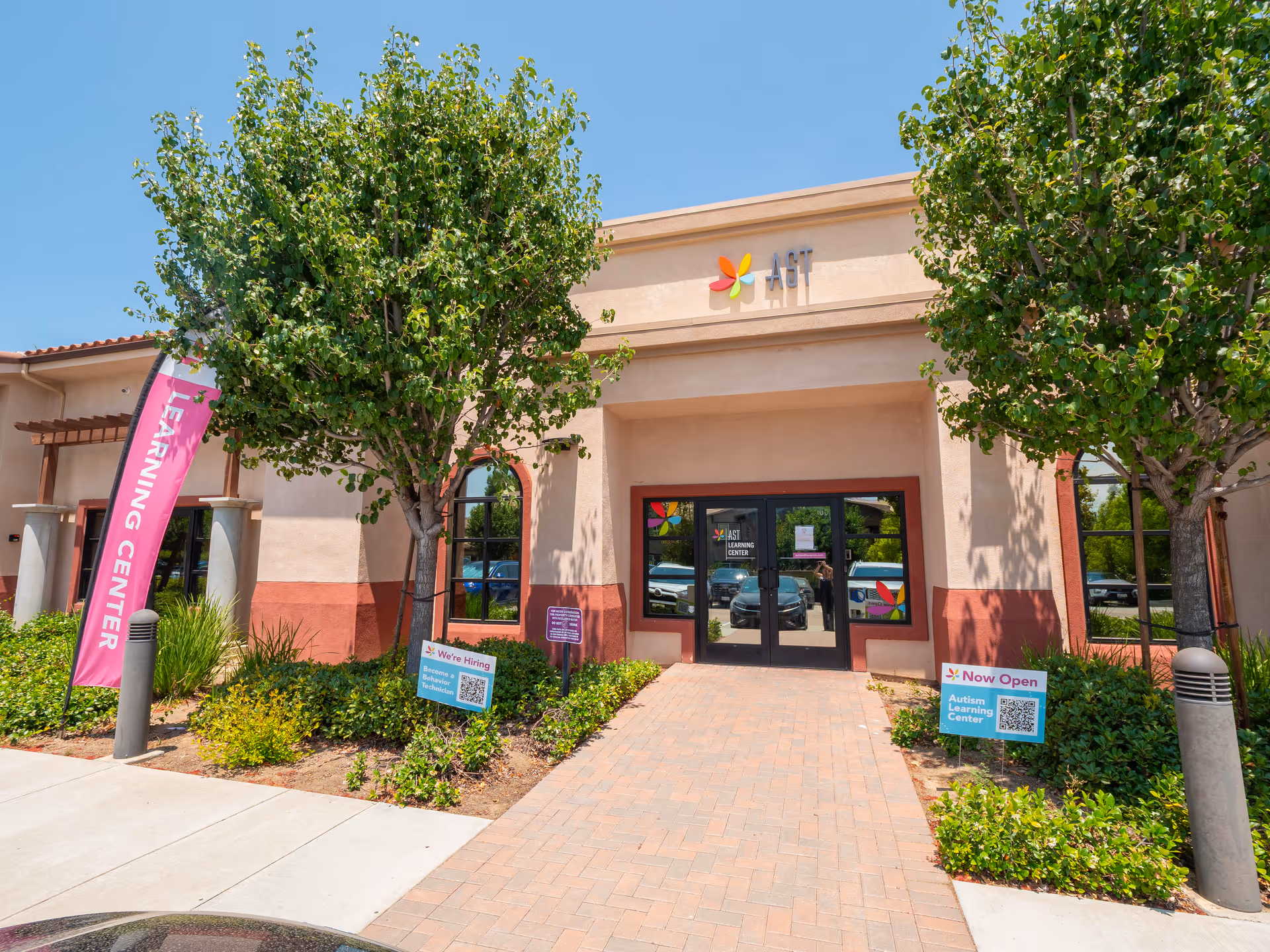 Front of an Autism Spectrum Therapies building with glass doors, trees, and colorful signage.
