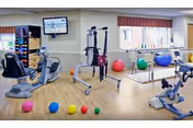Bright indoor therapy gym with treadmills, stationary bikes, and colorful exercise balls.