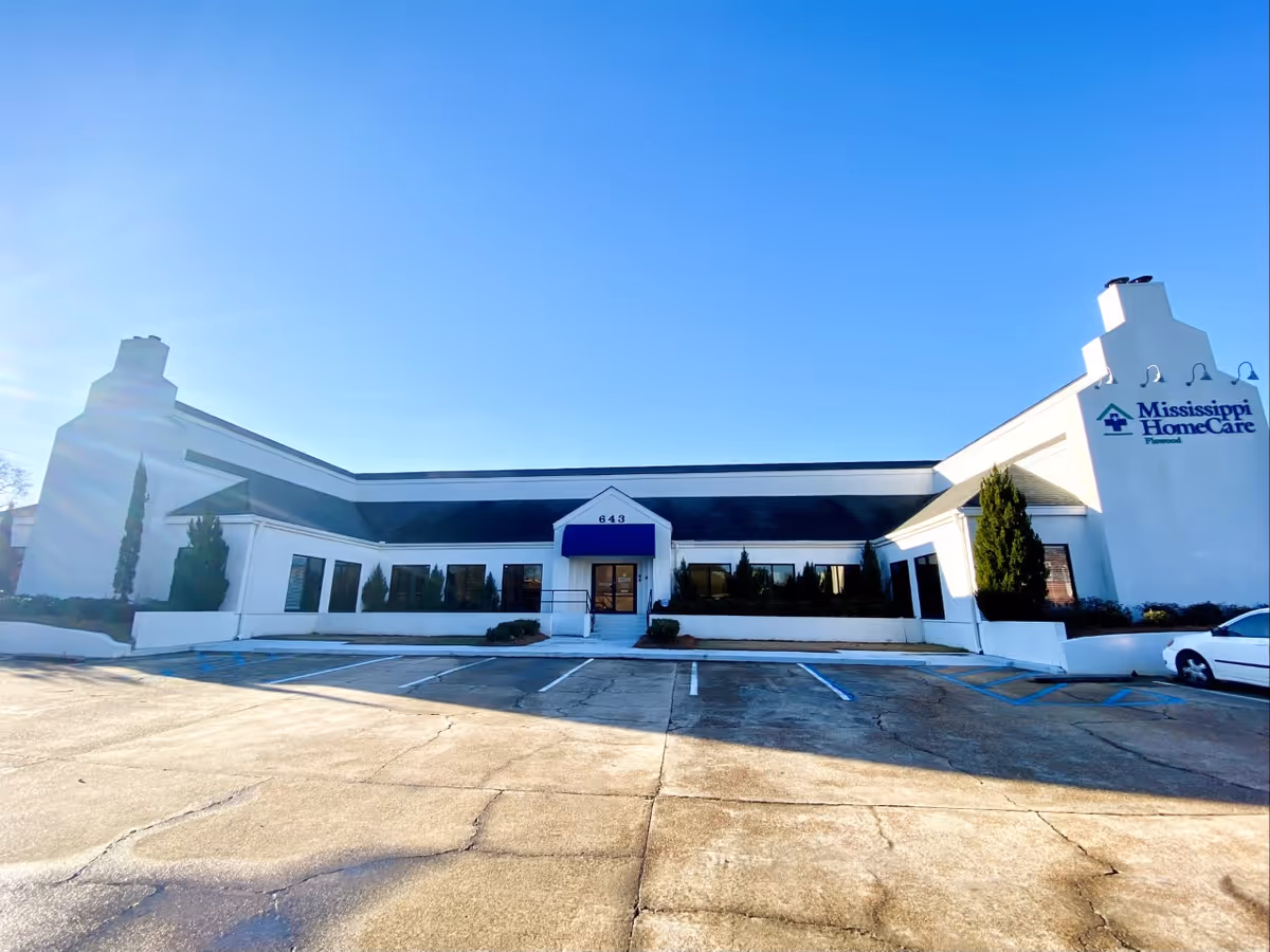 White single-story building with blue awning and Mississippi HomeCare sign, parking lot in front.