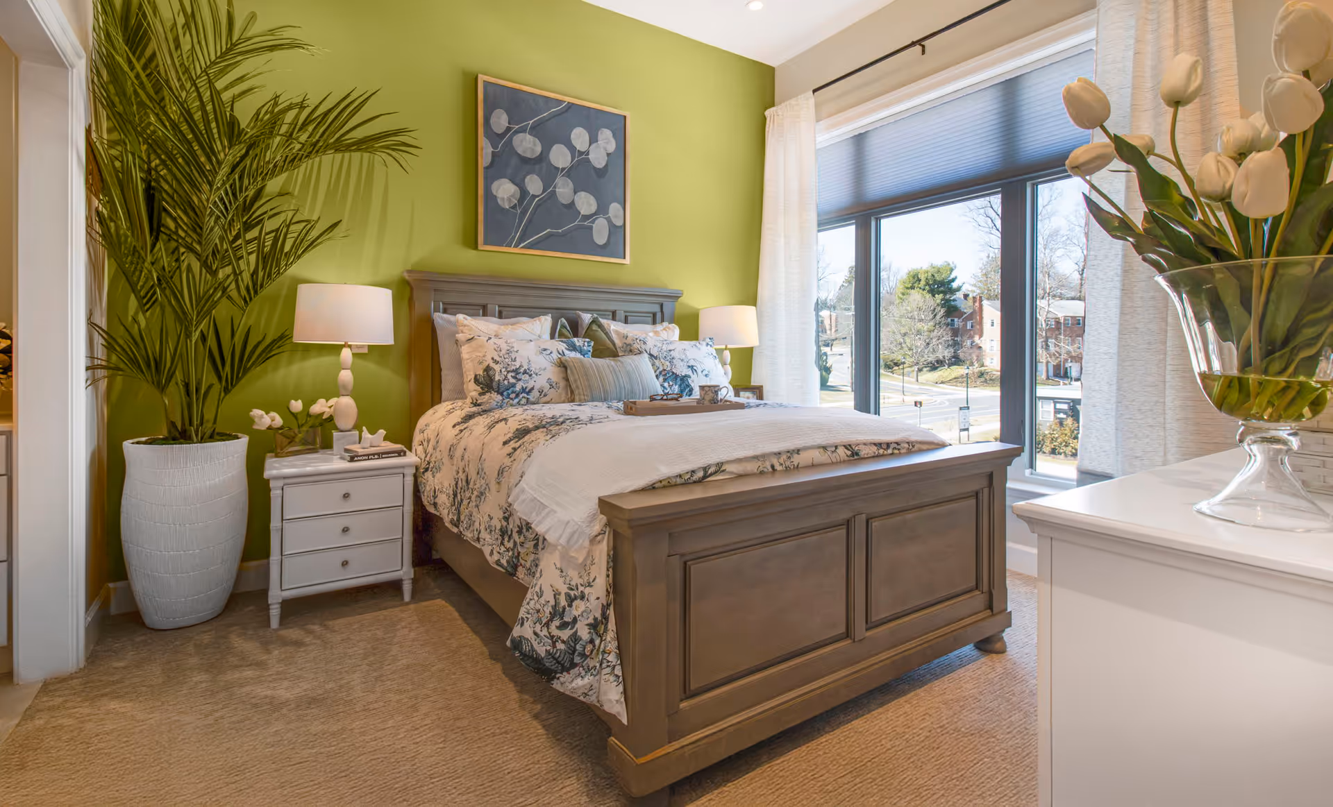 A well-appointed bedroom with a large wooden bed, green accent wall, and sunlit window.