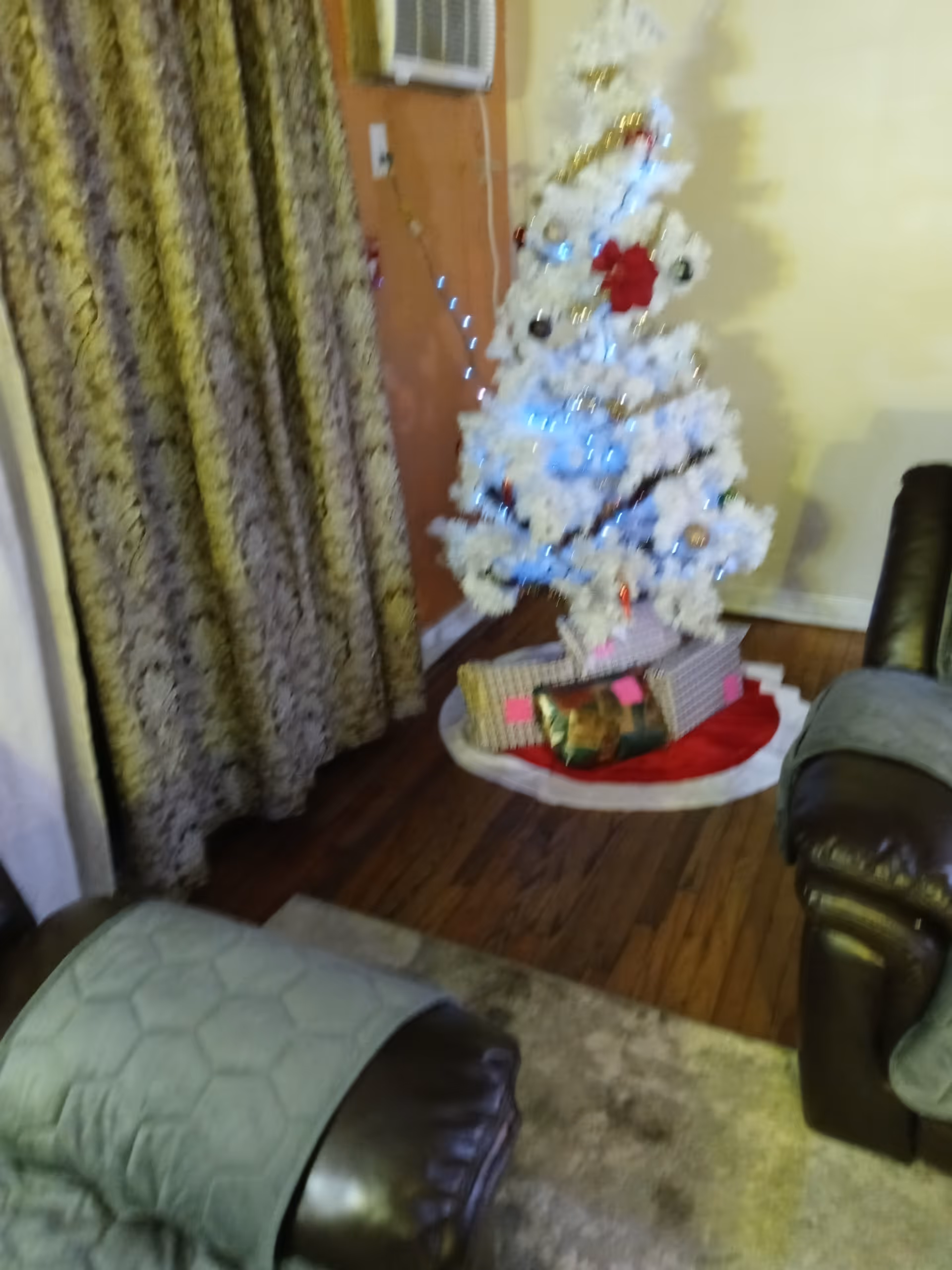 White Christmas tree with wrapped gifts sits in a living room beside brown leather chairs.