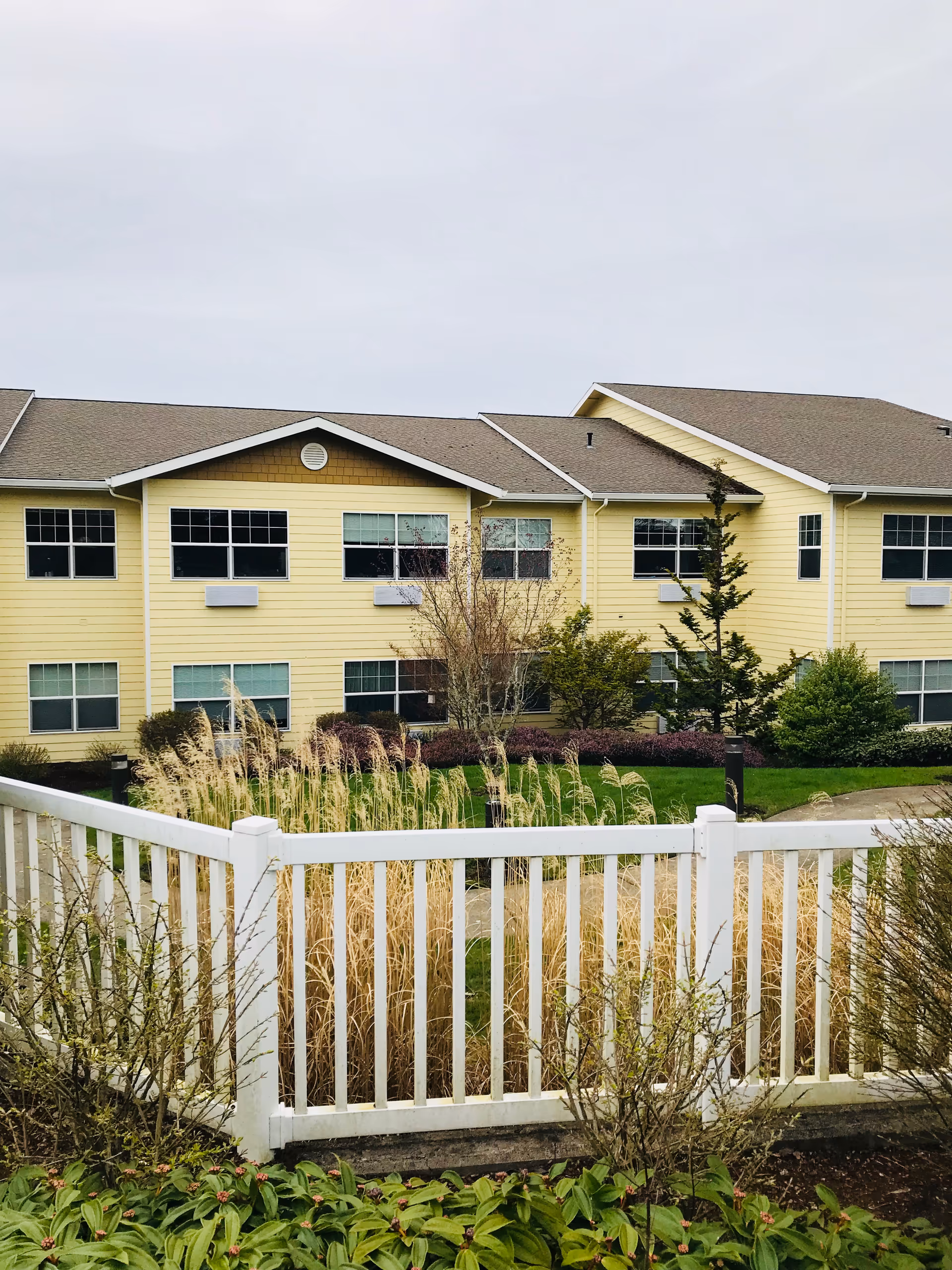 Yellow senior living building exterior with white fence and landscaped foreground.