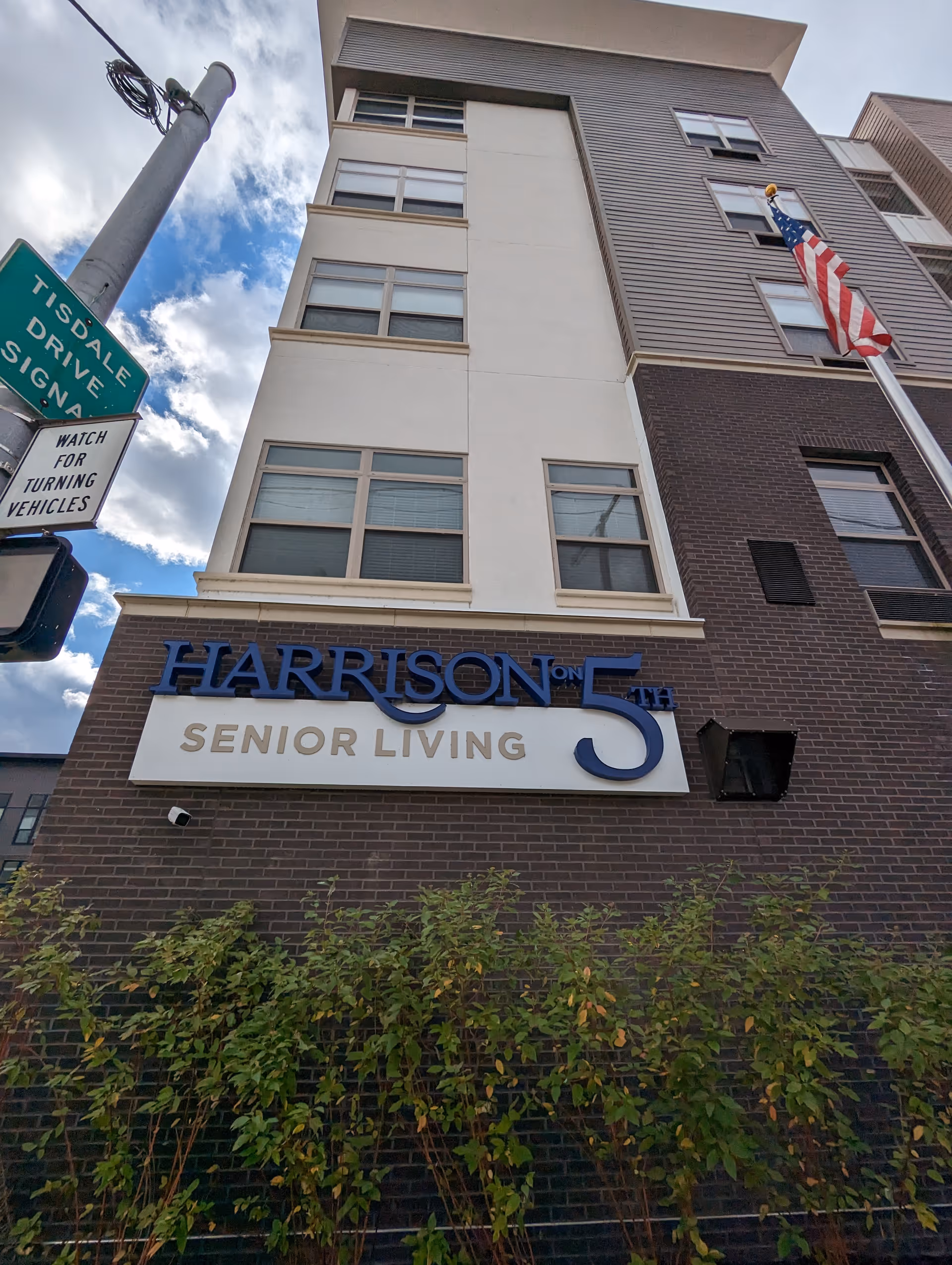 Exterior view of Harrison on 5th Senior Living building with sign and flag