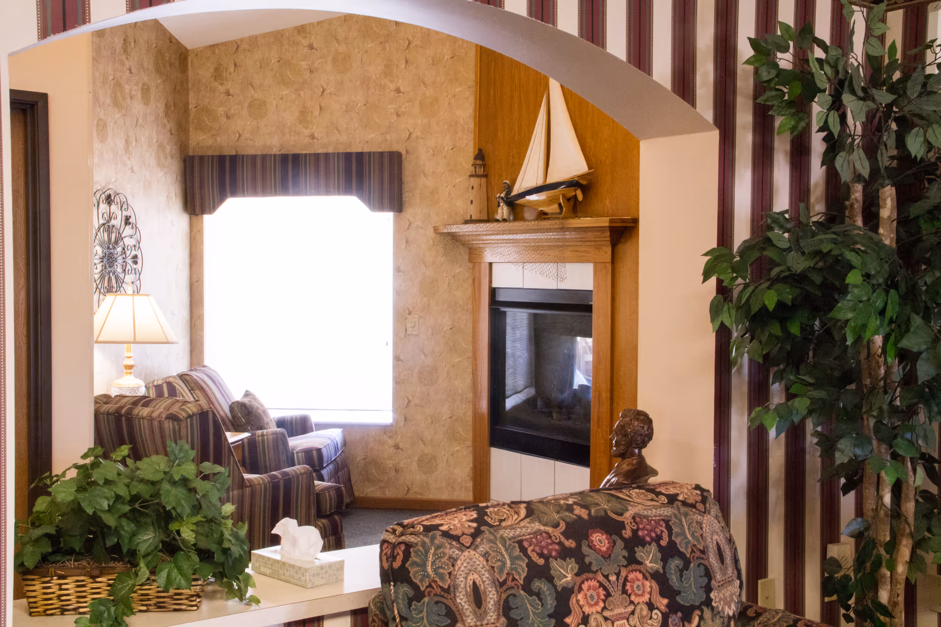 Cozy living room with archway, fireplace, striped seating, and potted plants.