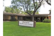 One-story brick building with a lawn and a sign reading "Pioneer Health Care Center" in front of a large tree.