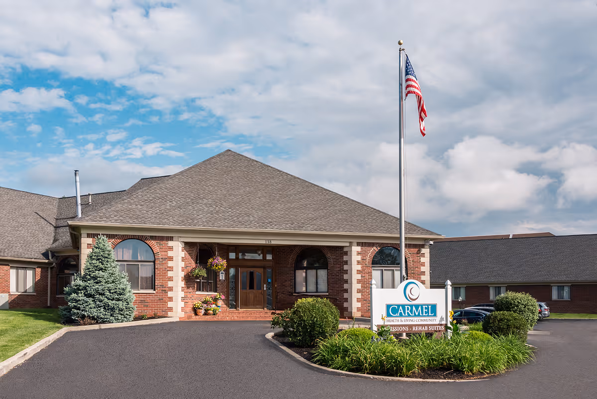 Brick senior living facility with flagpole, arched entrance, and manicured landscaping.