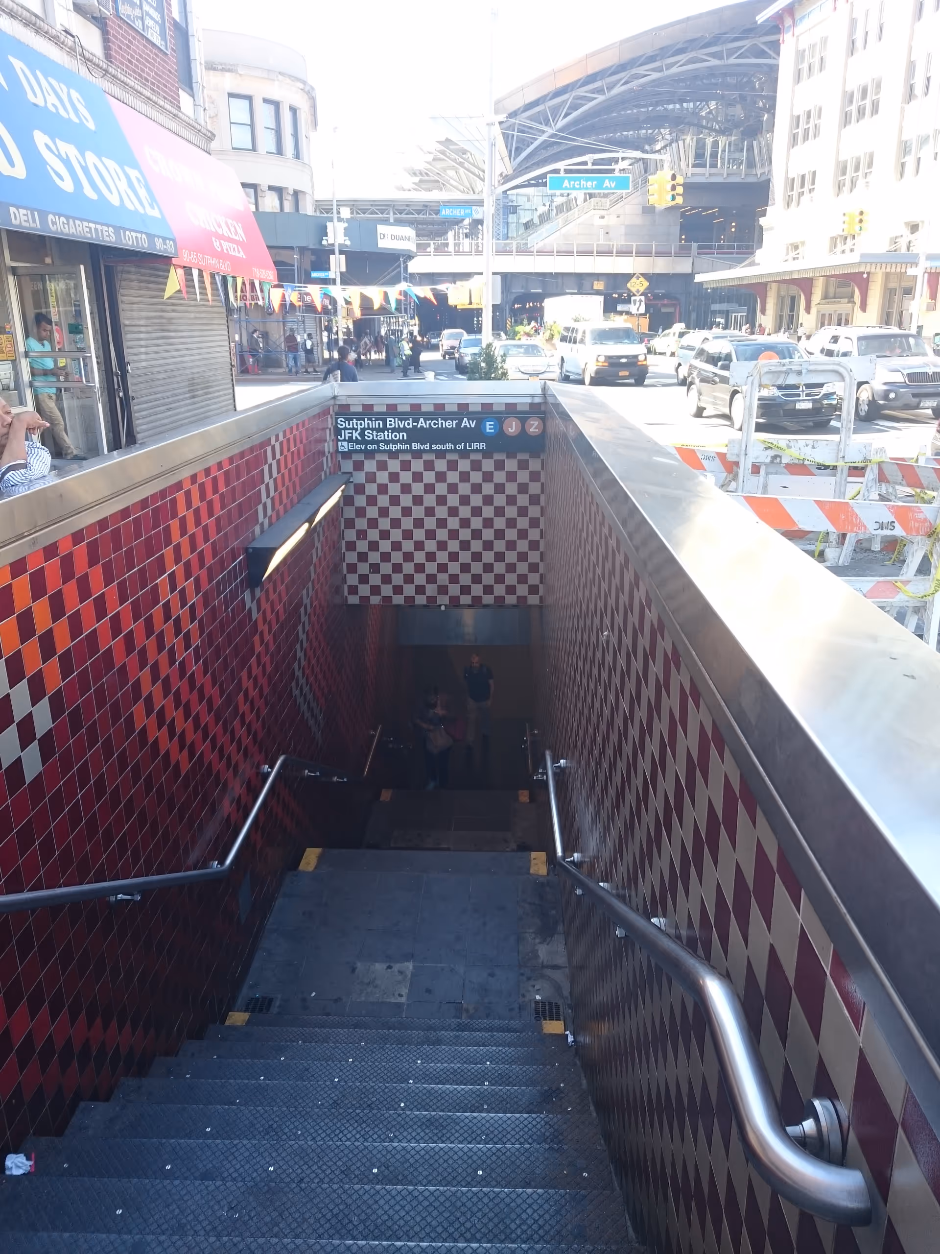 Subway entrance with red checkered walls, descending stairs, and pedestrians.