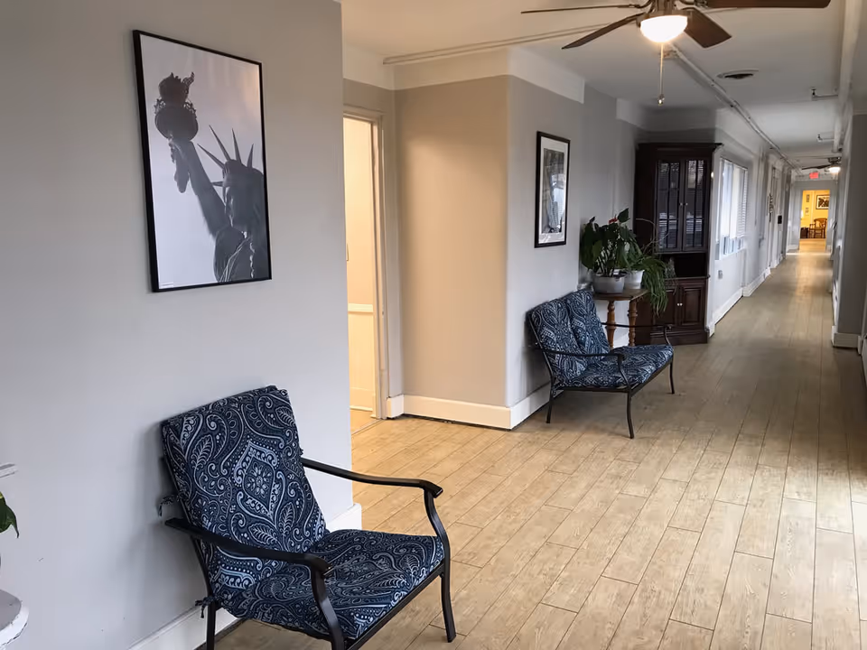 Hallway of a senior living facility with blue patterned chairs, plants, and wall art.