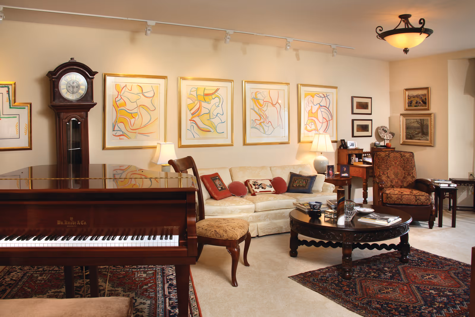 Well-appointed living room with a grand piano in the foreground, a sofa, armchair, coffee table, grandfather clock and framed artwork on the wall.