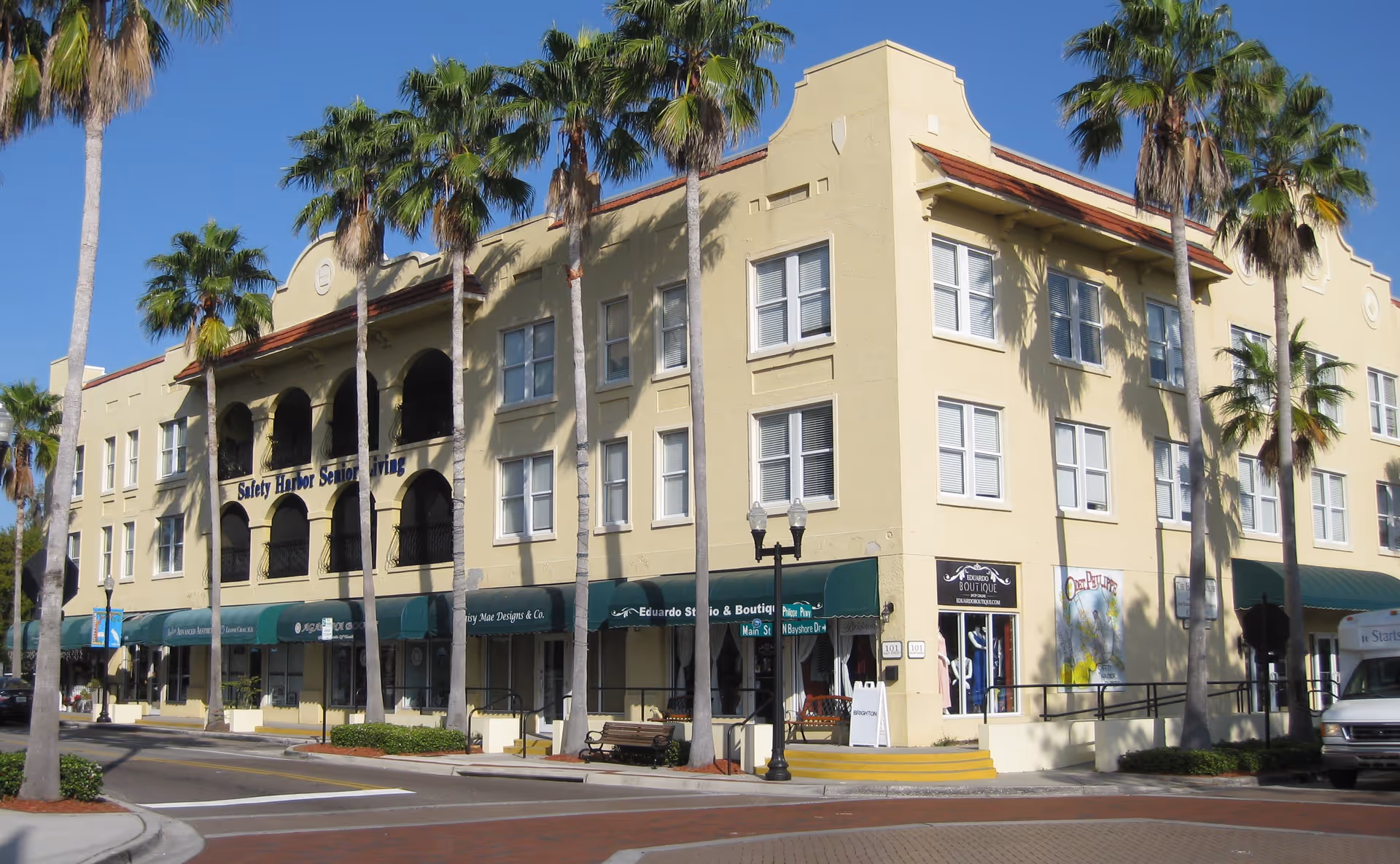 Three-story beige building labeled Safety Harbor Senior Living on a sunny street with palm trees.