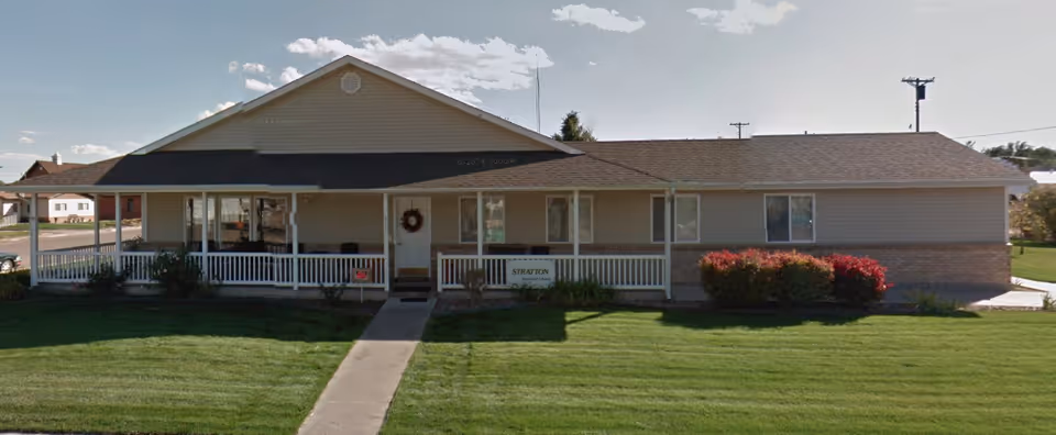 Front view of a single-story assisted living facility with a wrap porch and green lawn.