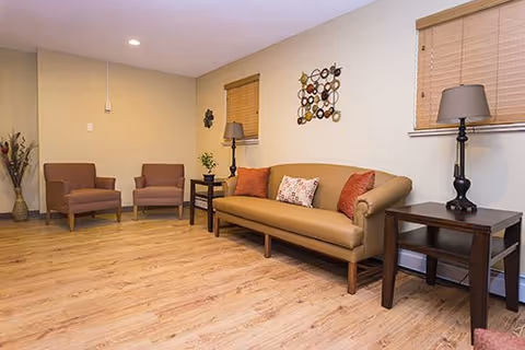 Cozy senior living lounge with sofa, chairs, lamps, and wall decor