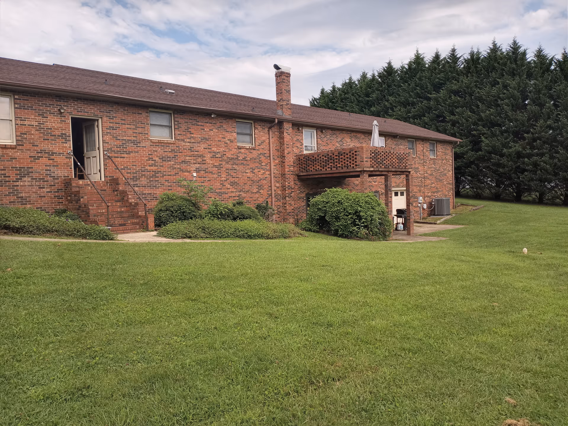 Brick TLC Family Care Home exterior with green lawn, stair entry, and balcony.