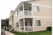 Two-story beige Lakeside Village Apartments building with balconies and a green lawn.