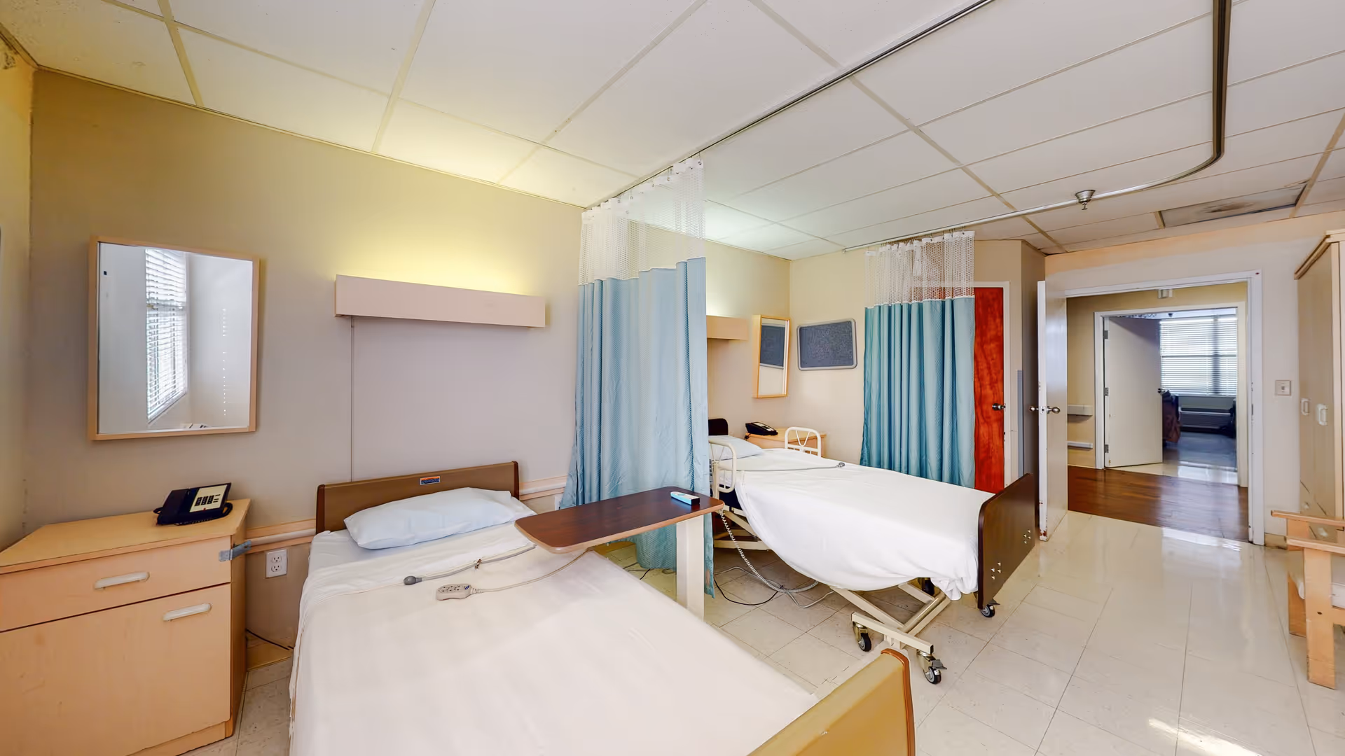 Two hospital beds with privacy curtains in a bright shared patient room.