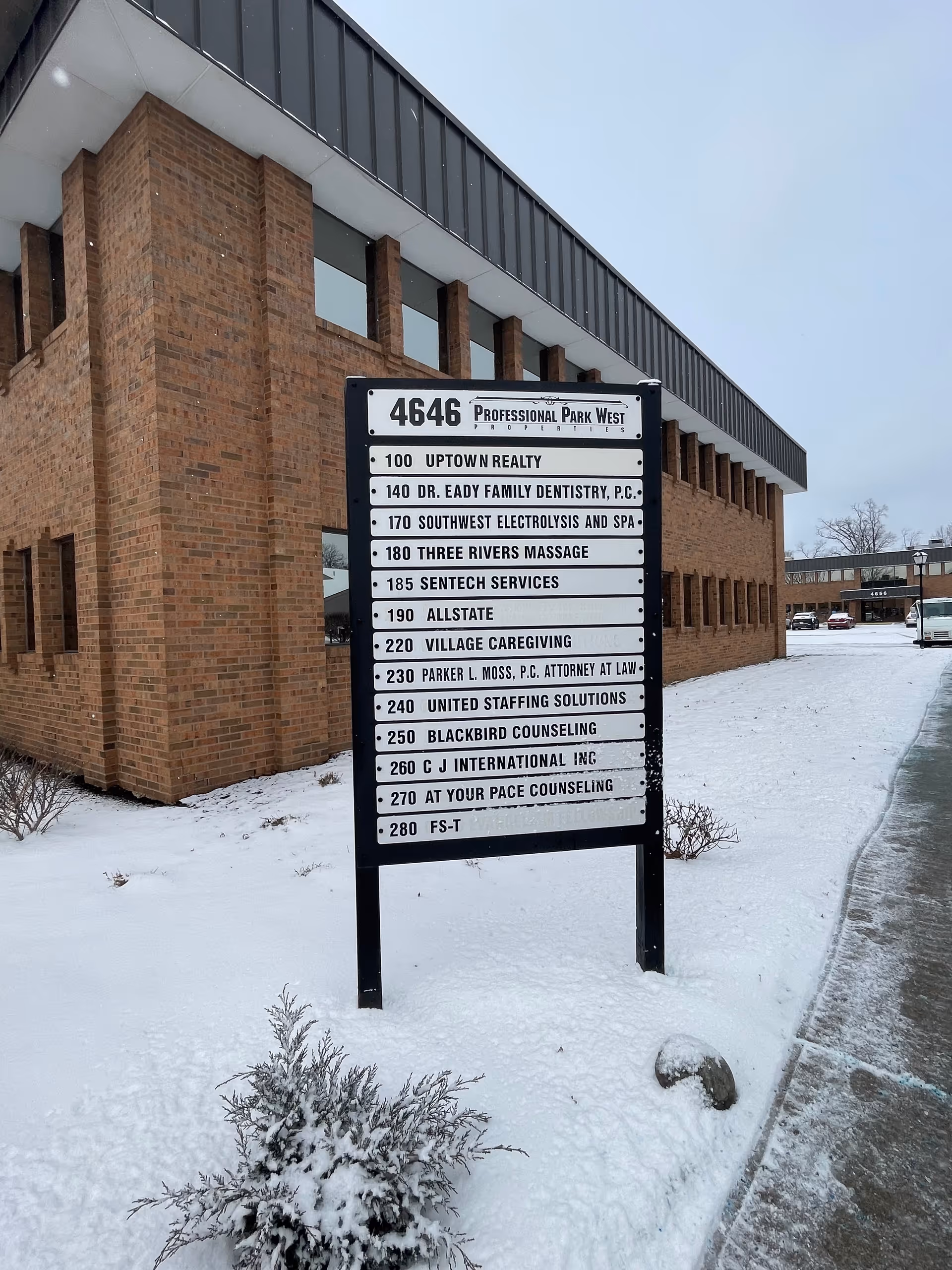 Brick commercial building with a tall directory sign listing Village Caregiving and other businesses.