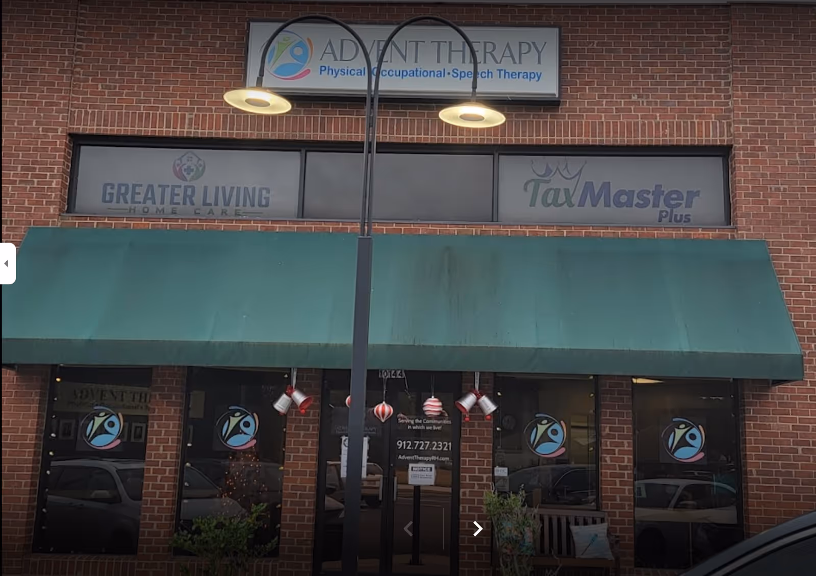 Brick storefront with a green awning and signs for Greater Living Home Care.