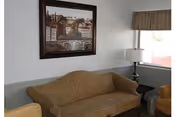 A small living area with a patterned sofa, lamp, wall art, and window.