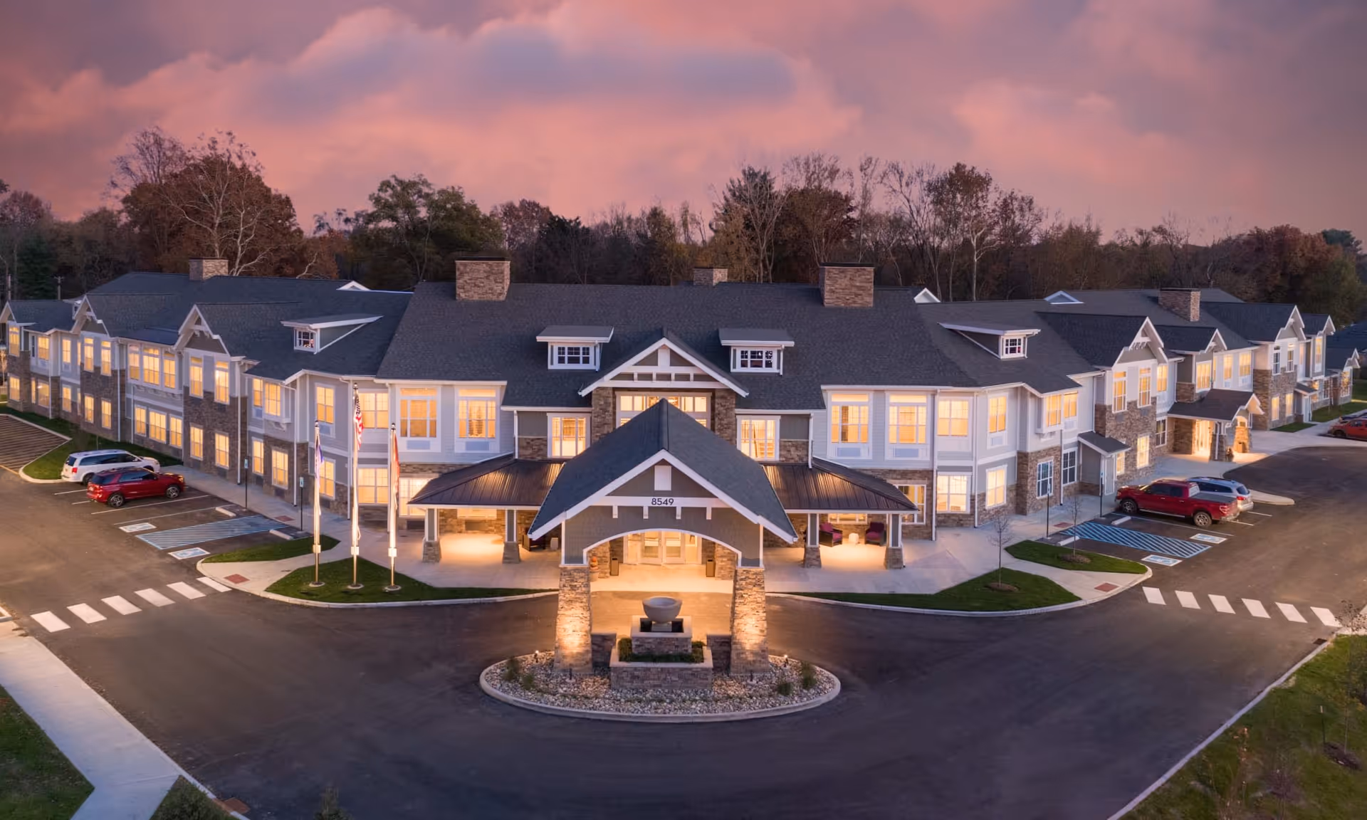 A large senior living campus with a curved entrance, driveways, and warm lights at dusk.