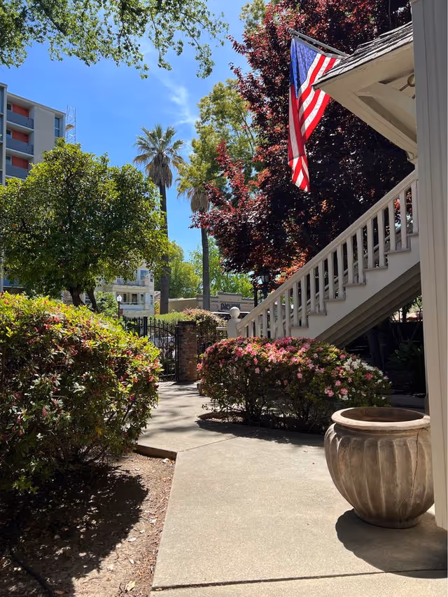 Outdoor facility entrance with stairs, American flag, and blooming shrubs.