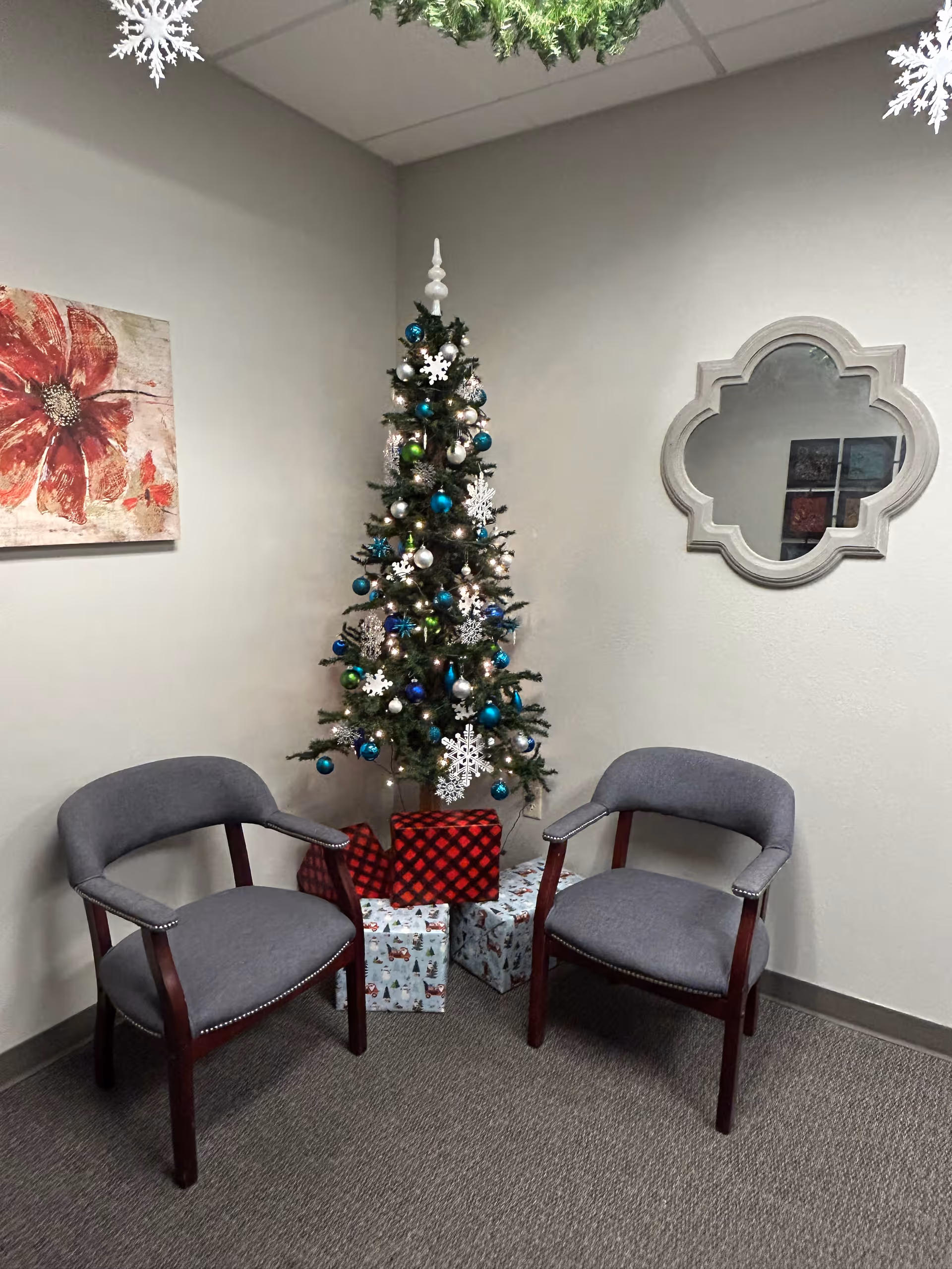 Corner waiting area with a Christmas tree, chairs, and wrapped gifts.