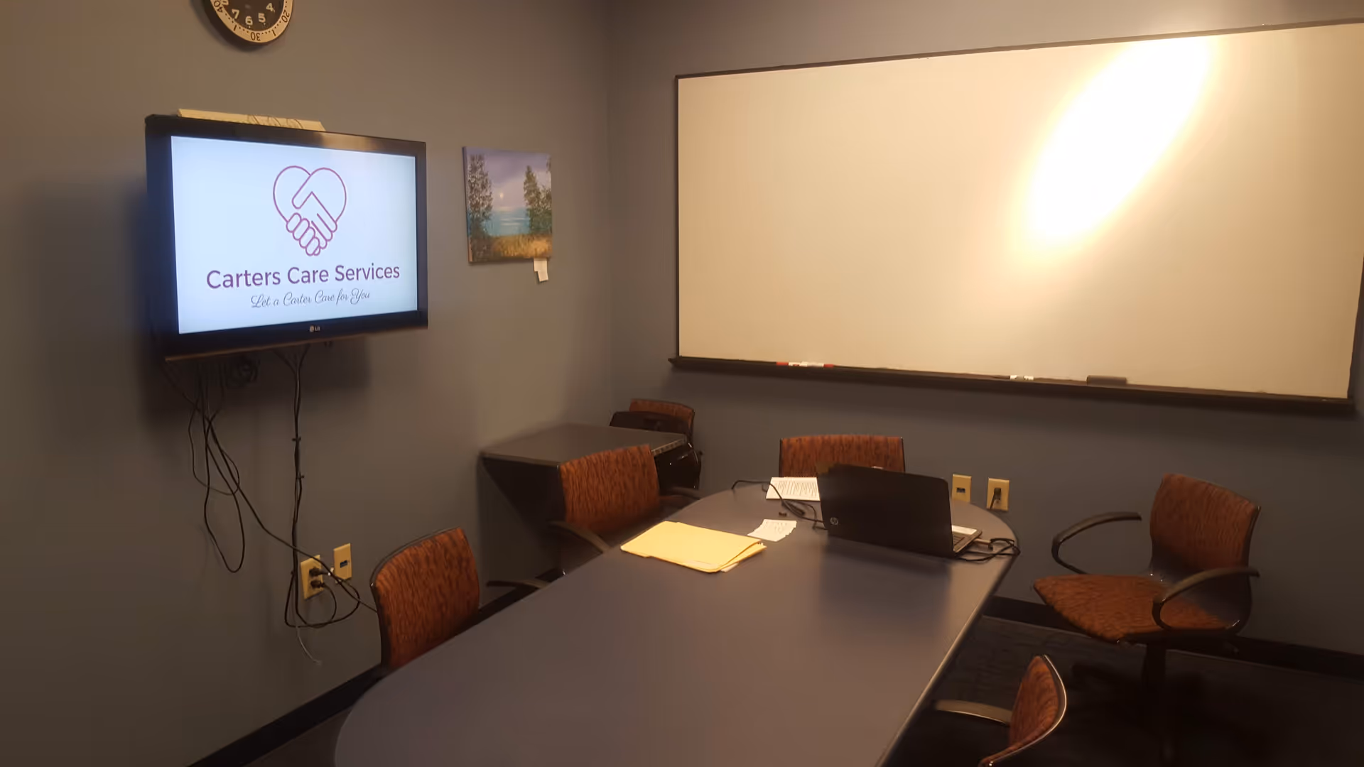 Small conference room with a table, chairs, whiteboard, and a TV displaying Carters Care Services logo.