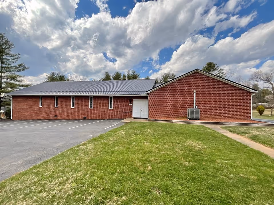 Red brick, single-story building with metal roof, adjacent parking lot, and green lawn.
