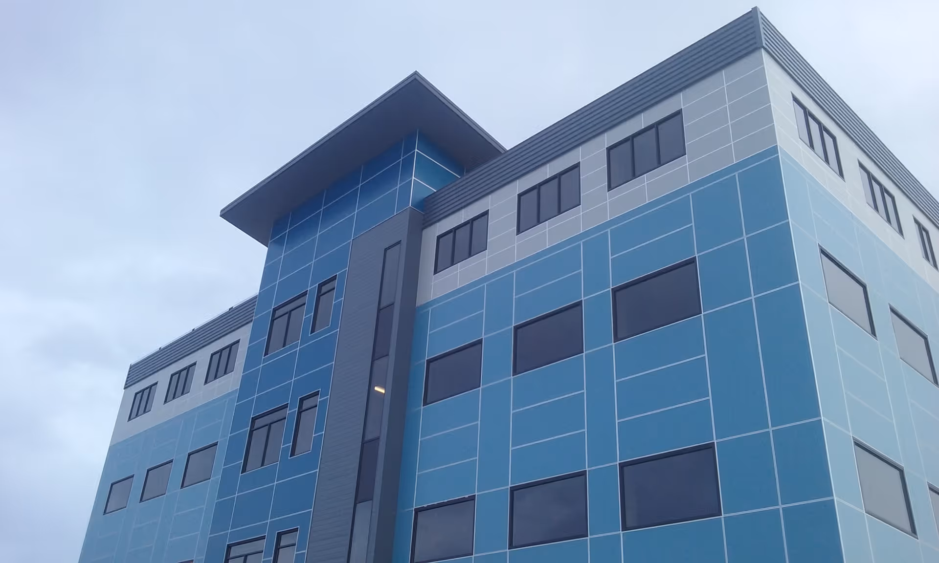 Modern blue-paneled multi-story building exterior against a cloudy sky.