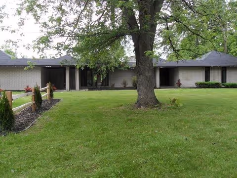 Single-story brick senior living facility with a manicured lawn and large tree in front.