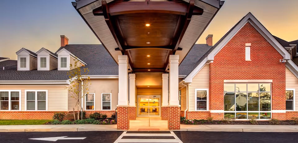 Front entrance of a brick-and-siding senior living facility with a covered drop-off canopy and large windows.