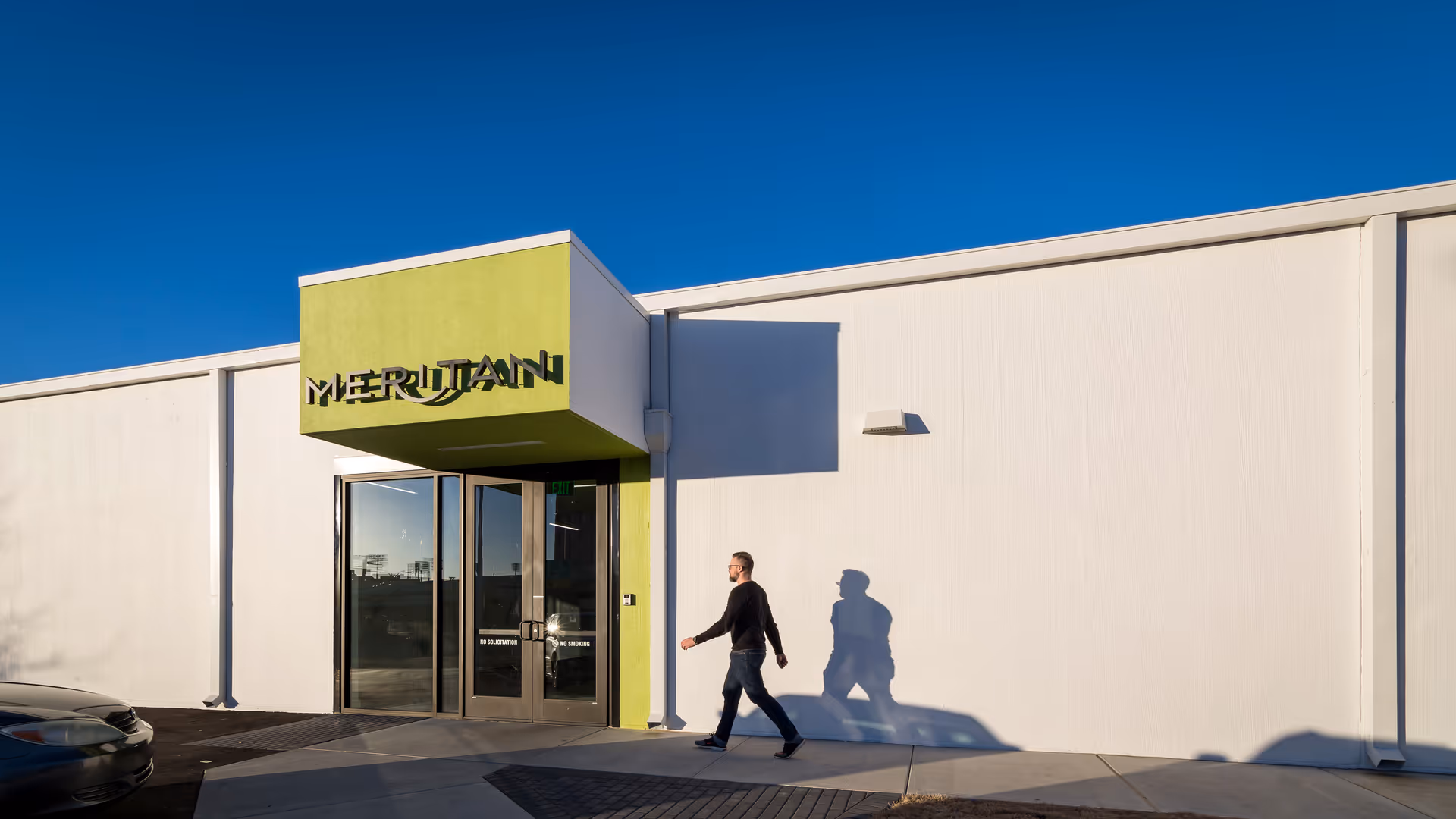 Exterior view of Meritan facility with lime-green entrance, glass doors, and a person walking.